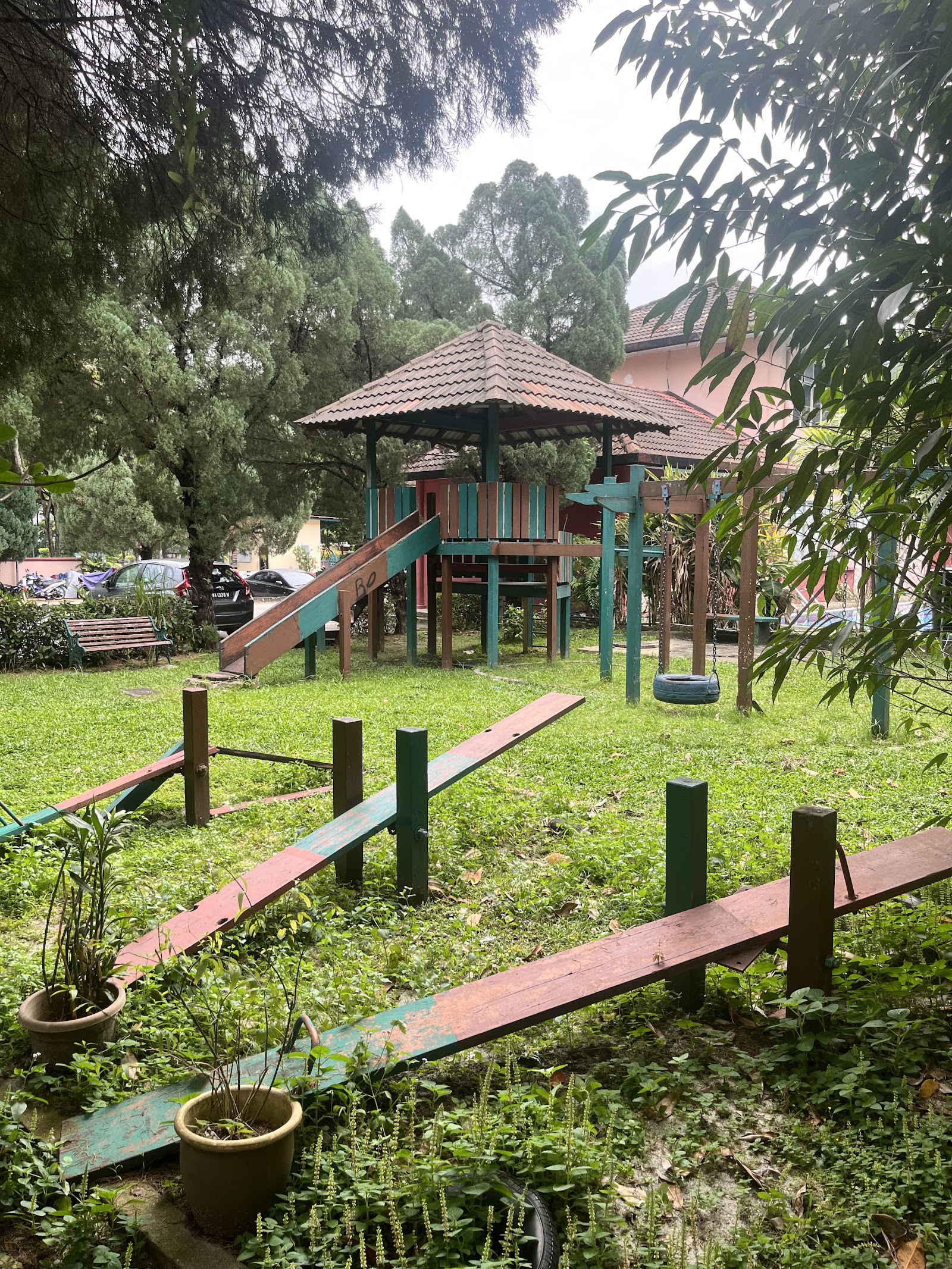 Pangsapuri Kayangan: A residential complex's outdoor children's play area featuring a wooden playground structure, see-saws, and a tire swing on a grassy lawn.