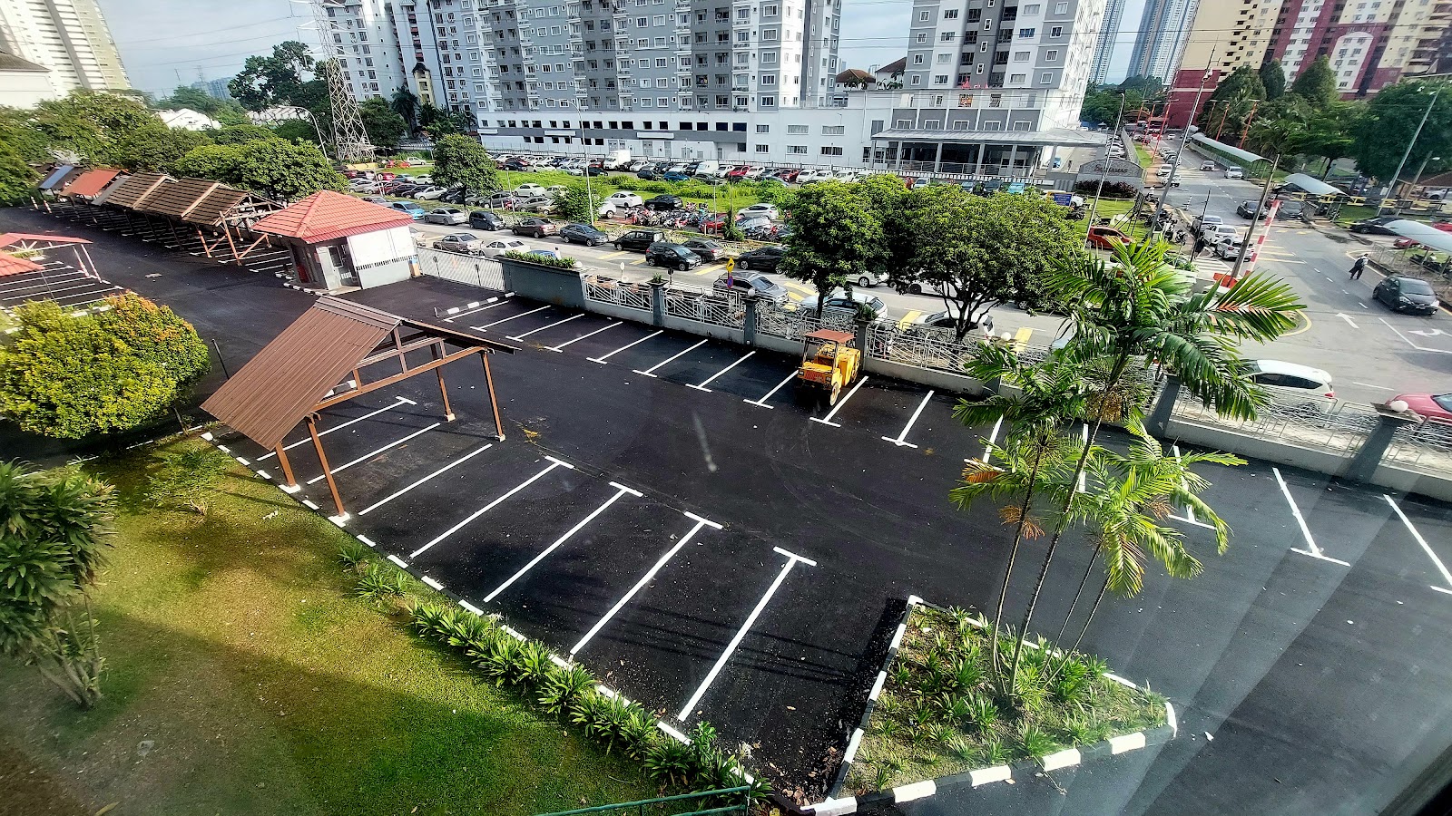 Ridzuan Condominium: Aerial view of a car park with white markings, a small shelter structure, and landscaping, with apartment buildings in the background.