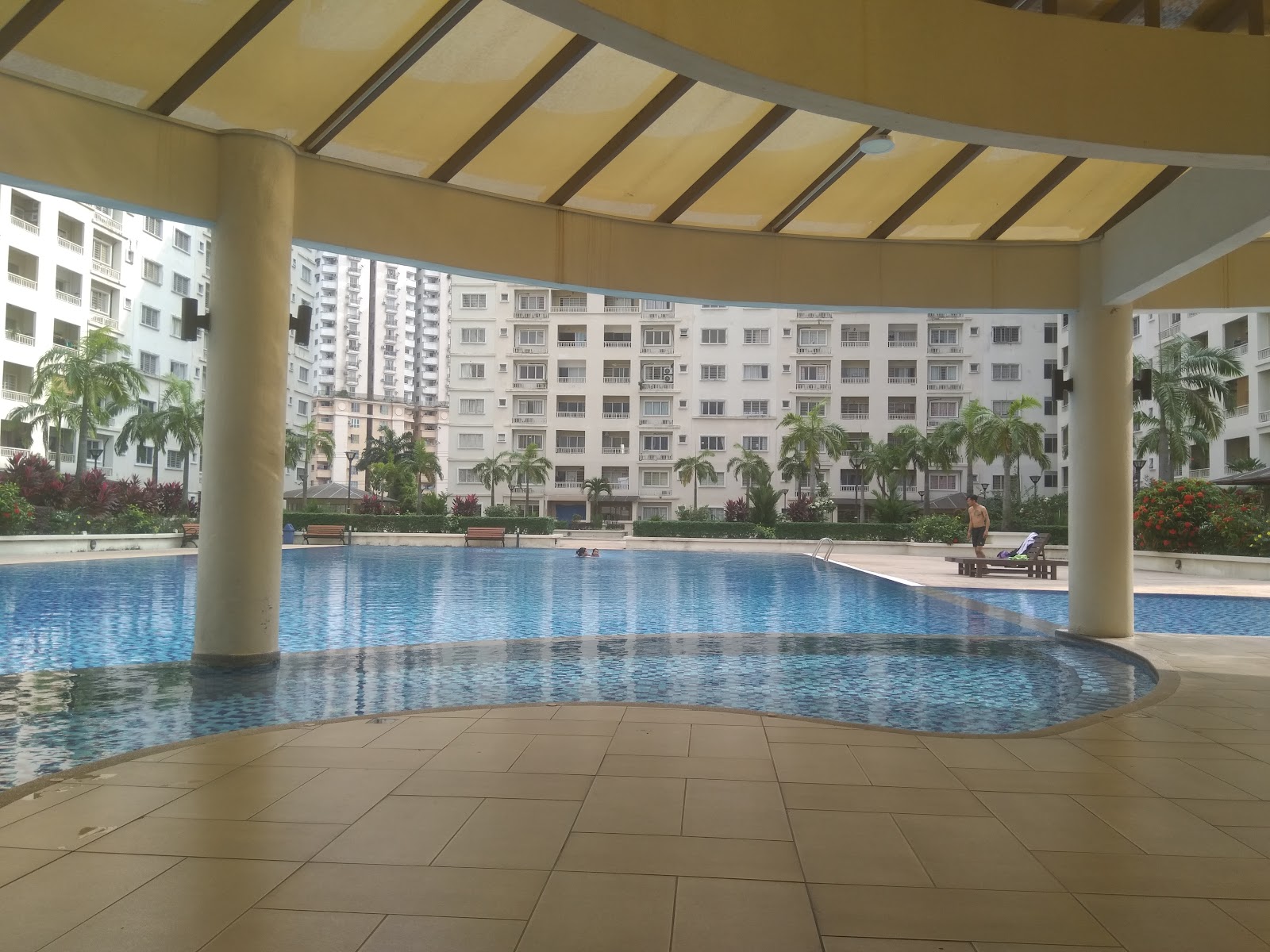 Suriamas: A residential swimming pool with a sheltered pergola in the foreground, surrounded by landscaped gardens and apartment buildings.