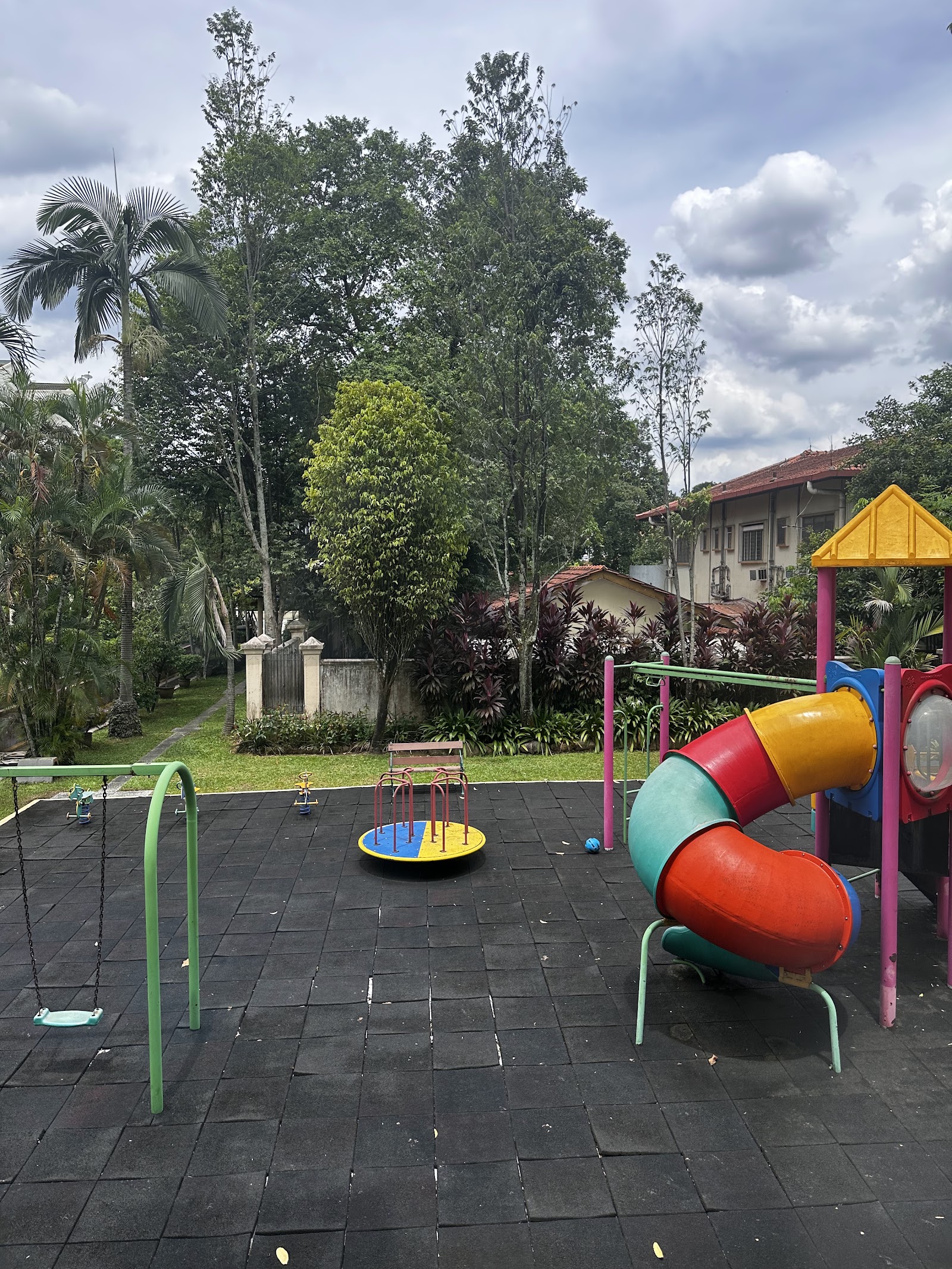 Regal Villa: A children's playground featuring a colorful slide, swings, and a spinning disc, set on a safety surface with trees and a building in the background.