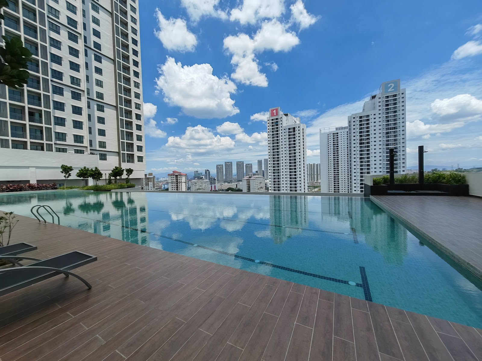 Residensi Bintang Bukit Jalil: A rooftop infinity pool with a wooden deck and sun loungers, reflecting the sky and surrounding residential towers.