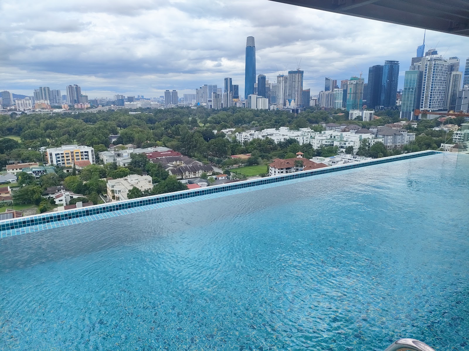 Residensi R8, Ampang Hilir: A view from an outdoor infinity pool overlooking a residential area and the city skyline under a cloudy sky.