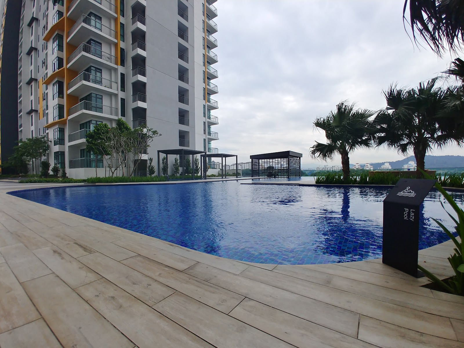Parkhill Residence Bukit Jalil: An outdoor infinity swimming pool decked in light stone tiles, flanked by palm trees and overlooking a residential high-rise.