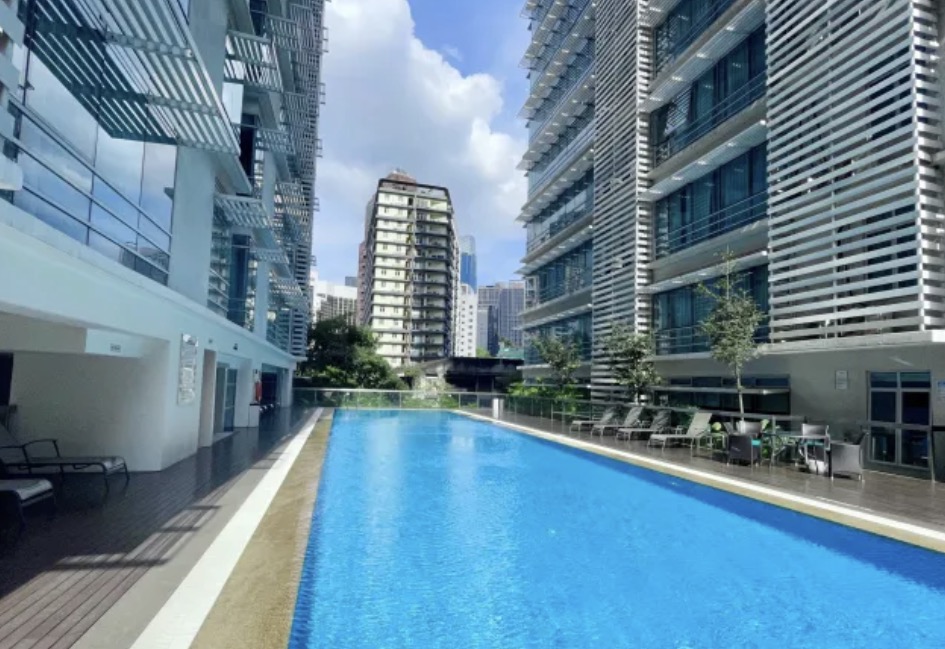 One Residency, KL: An outdoor swimming pool deck at One Residency KL, featuring blue water, lounge chairs, and flanked by the residential building facades.