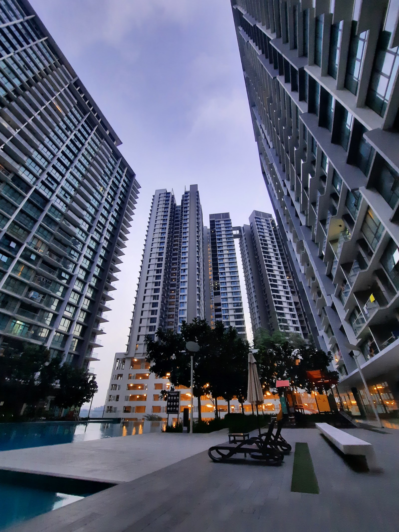 The Z Residence: A twilight shot of a swimming pool deck with lounge chairs and a closed umbrella, framed by several tall residential towers.