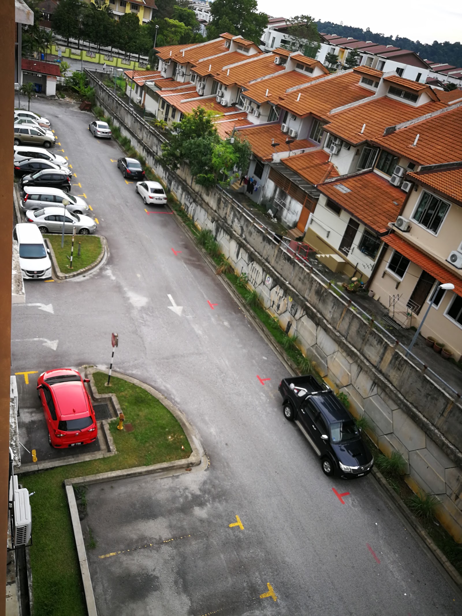 Pangsapuri Tainia: An elevated view of a street lined with terraced houses and a parking area with several cars.