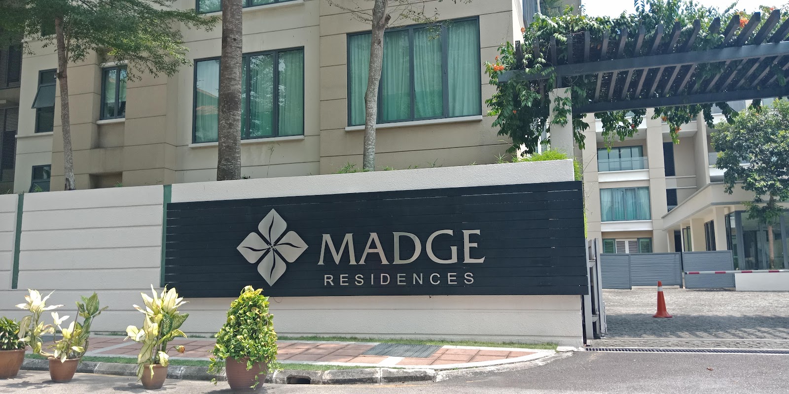 Madge Residences: The entrance signage wall of Madge Residences with the project logo and name, set against the background of the residential buildings and a gateway.