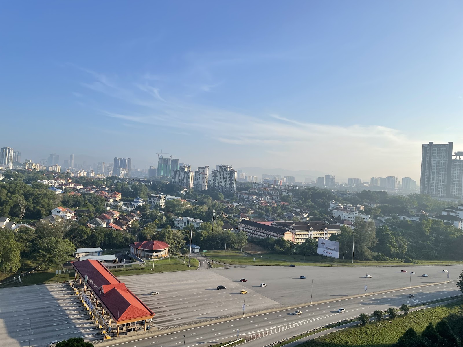 Casa Green: A wide, elevated cityscape view from a high vantage point, showing a residential area with detached houses, a bus terminal, and a highway in the foreground, with a distant skyline of high-rise buildings.