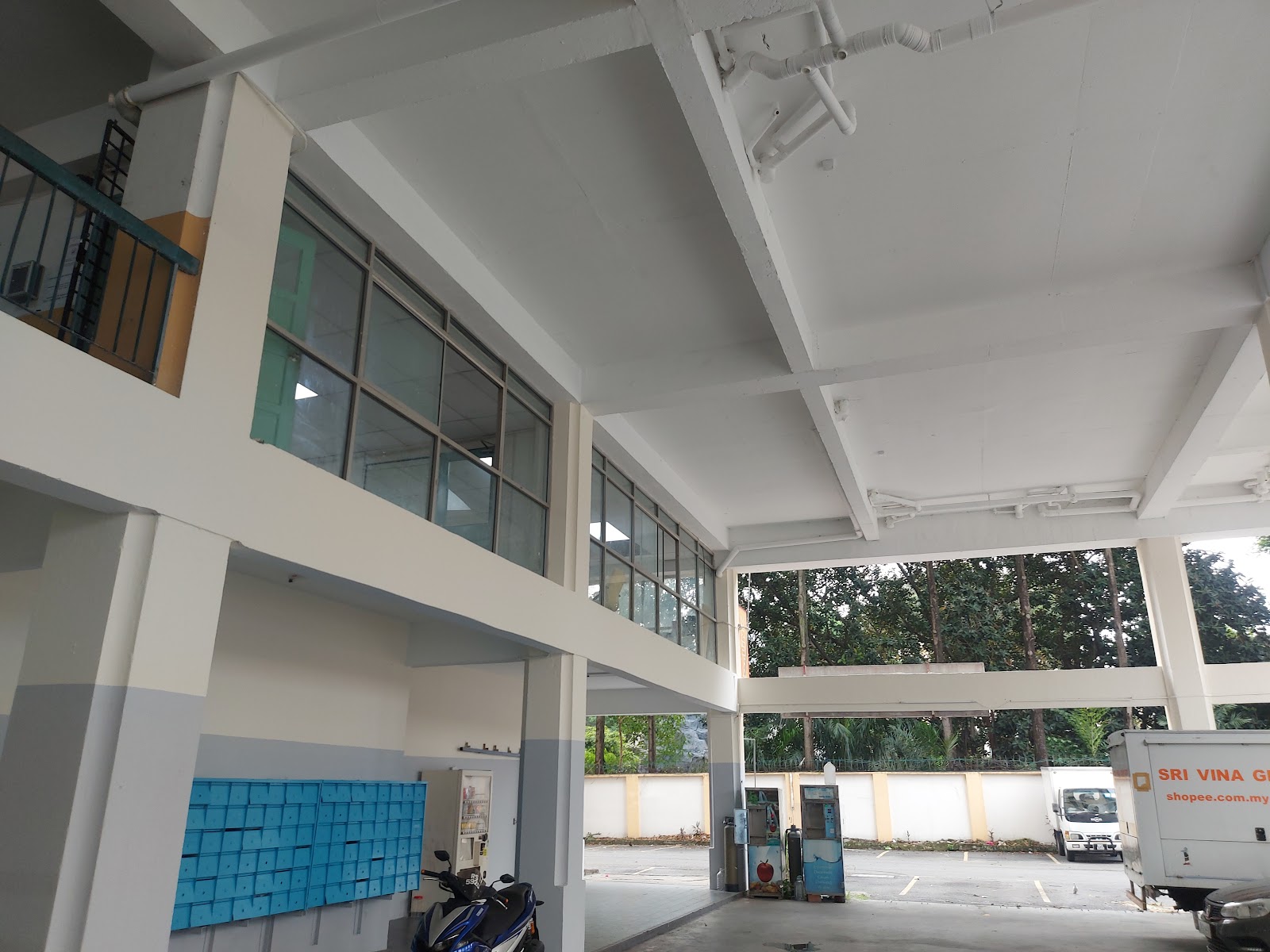 The Spectrum: The interior of a covered common area or drop-off zone with large windows, a wall of blue mailboxes, and a parked motorcycle.