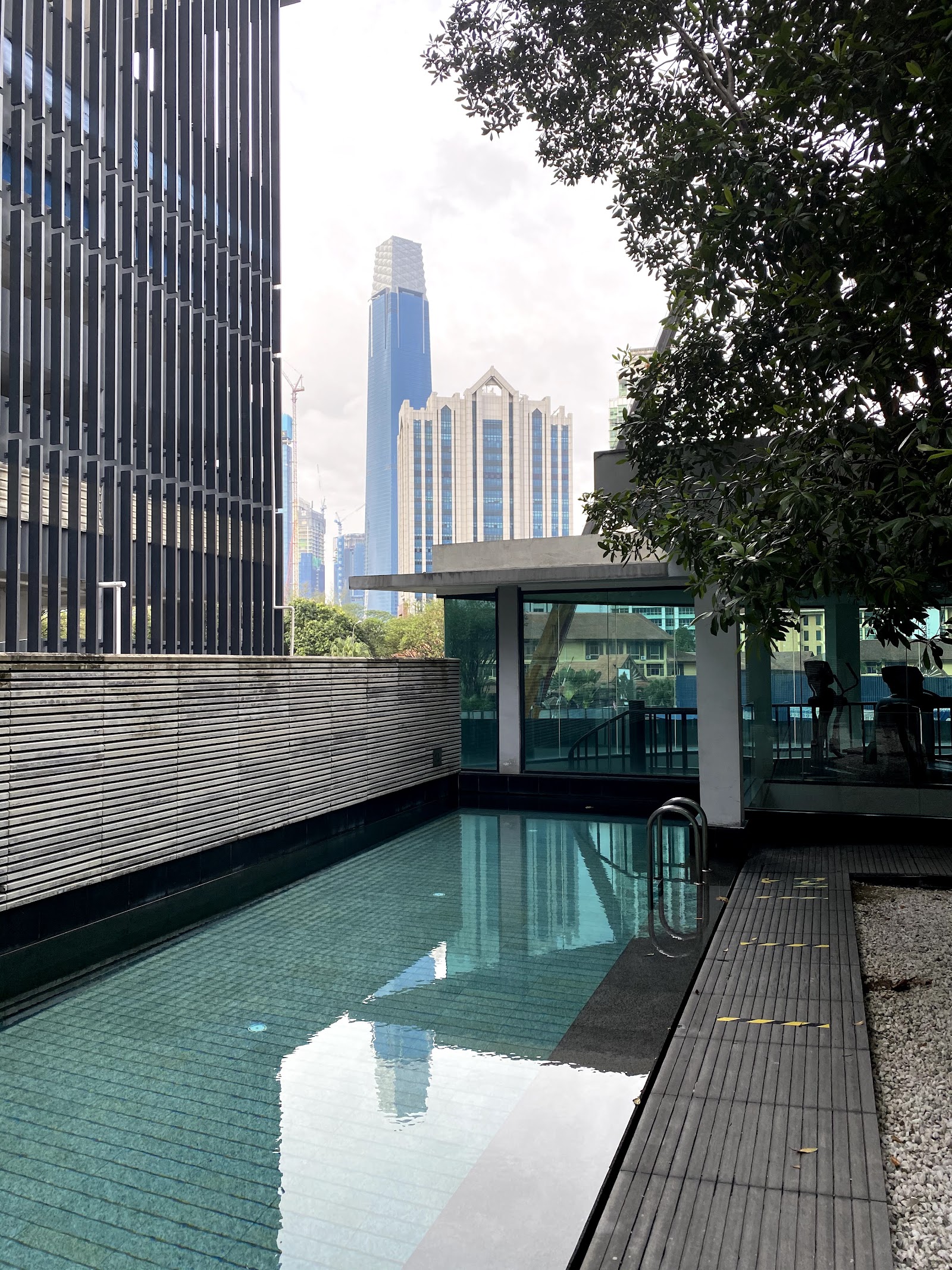 Ampersand: A swimming pool with a wooden deck and a glass-walled structure, overlooking a city skyline with modern skyscrapers.