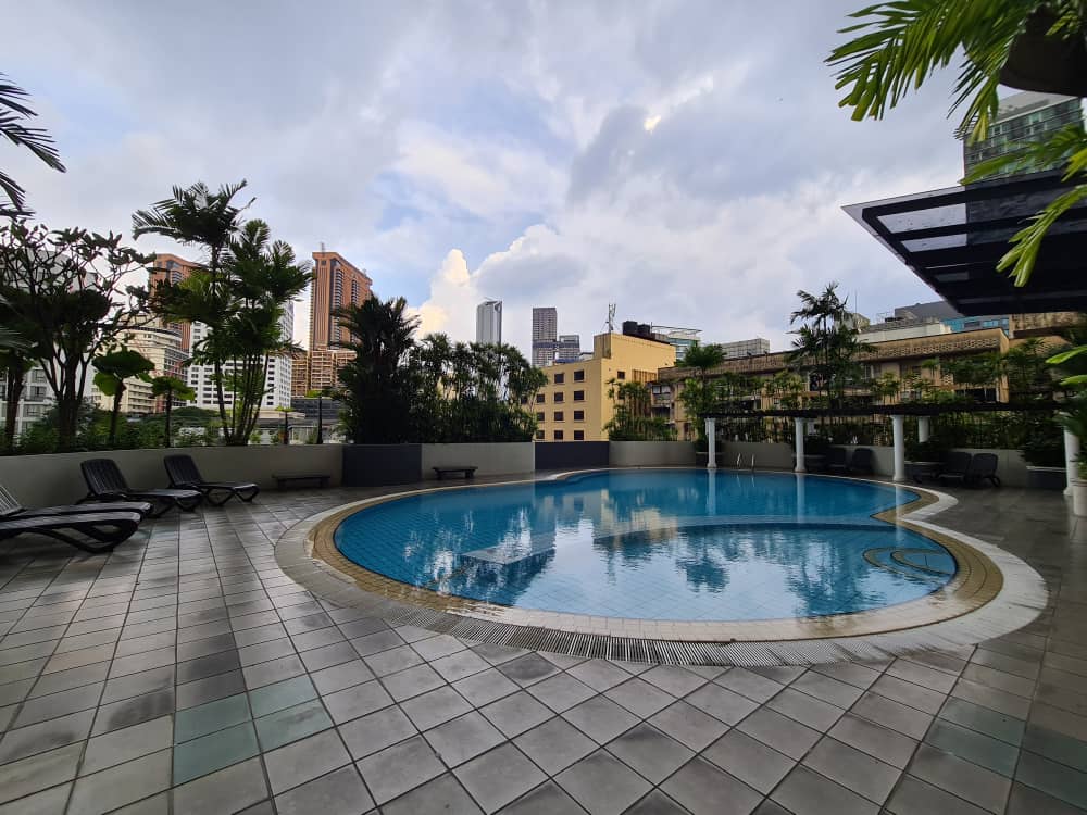 Angkasa Impian 1: A roof-top swimming pool with sun loungers and tropical plants, overlooking a city skyline.