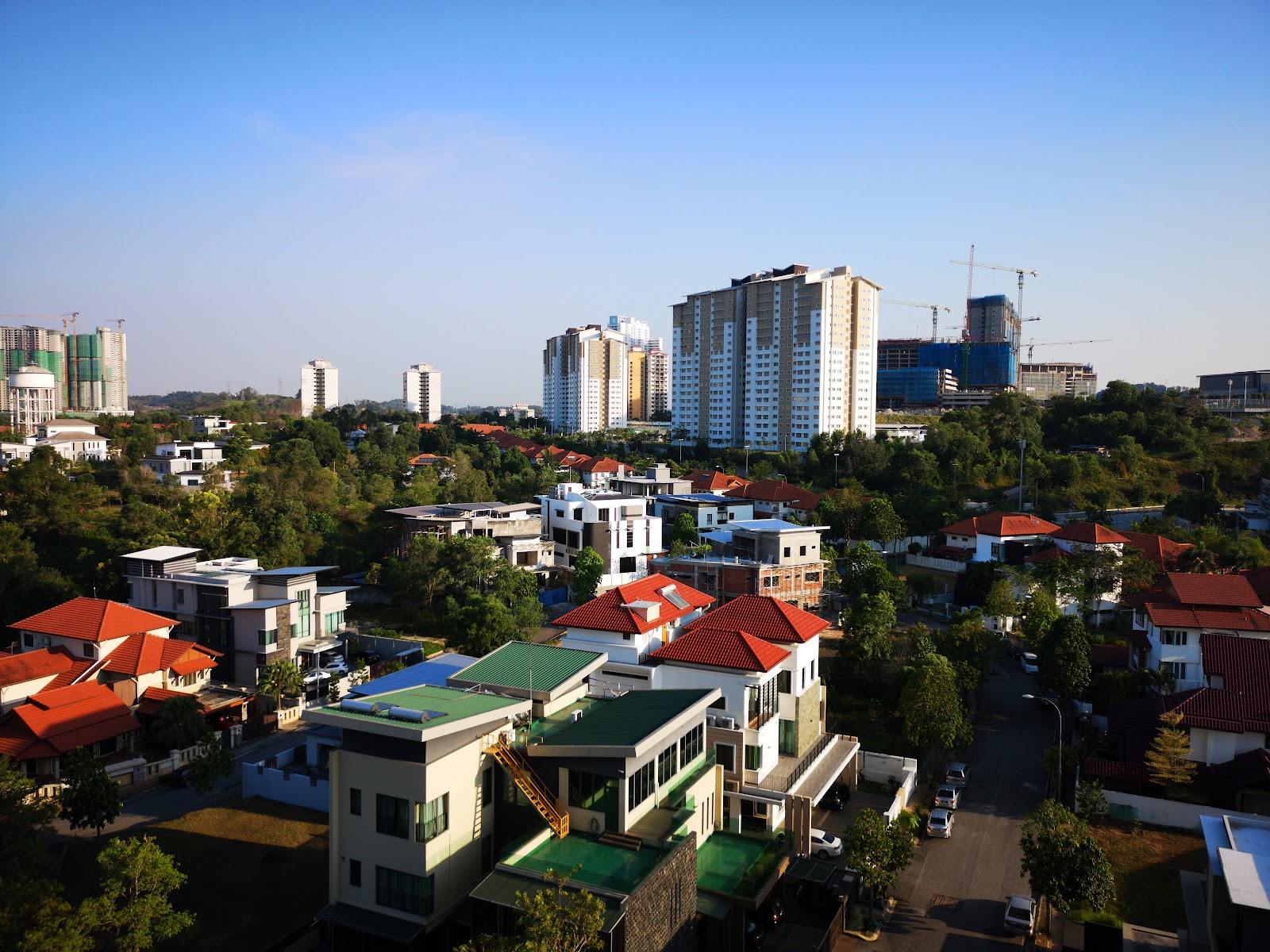 Denai Sutera: An elevated daytime view of a residential area with modern houses and apartment towers, overlooking a cityscape in the distance.