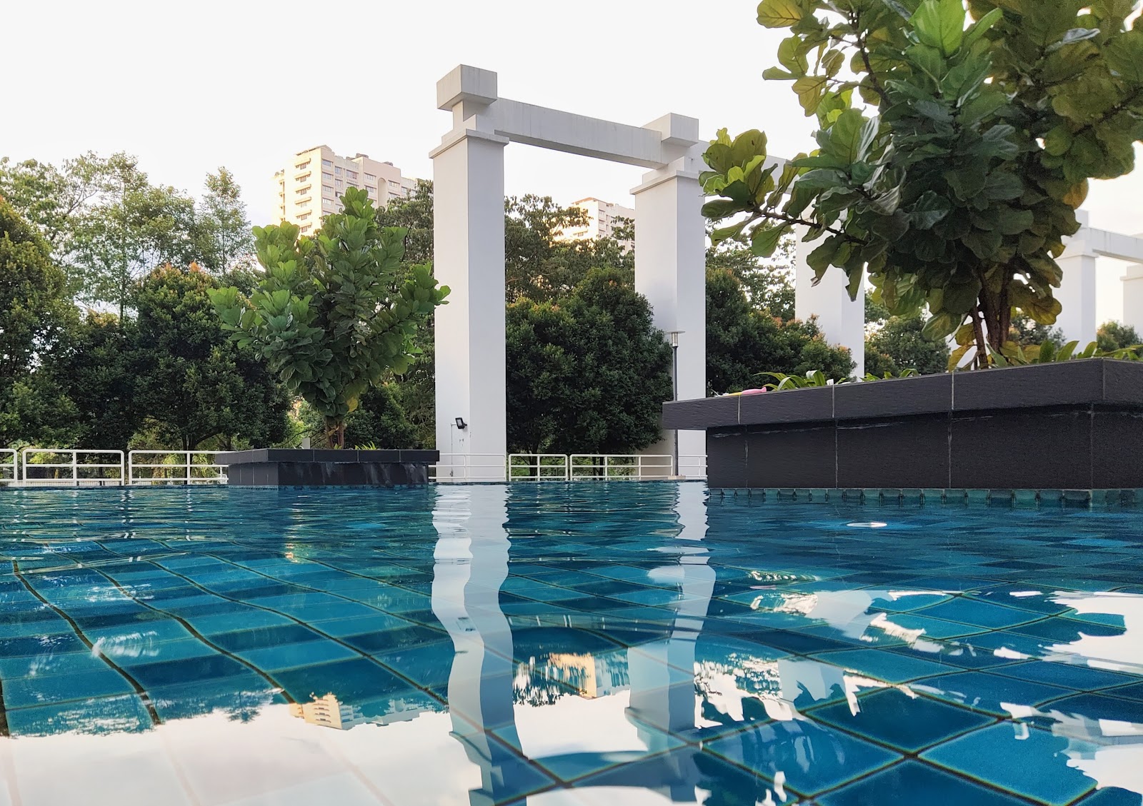 Kiara Residence 1: A rooftop swimming pool with blue tiles, featuring a white pergola structure and lush greenery in the background.