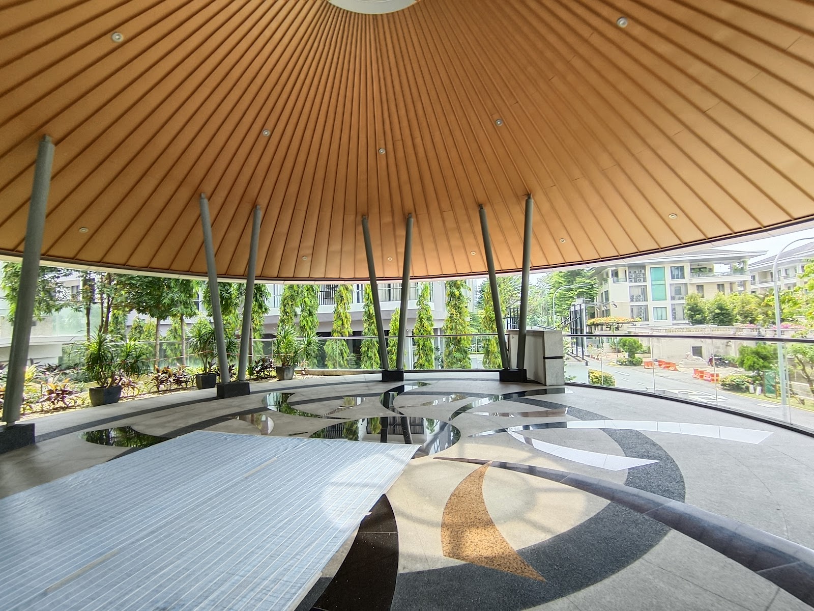 Gallery @ U-Thant: A covered circular pavilion or sky lounge with a wood-slat ceiling and patterned floor, looking out over landscaping and a residential building.