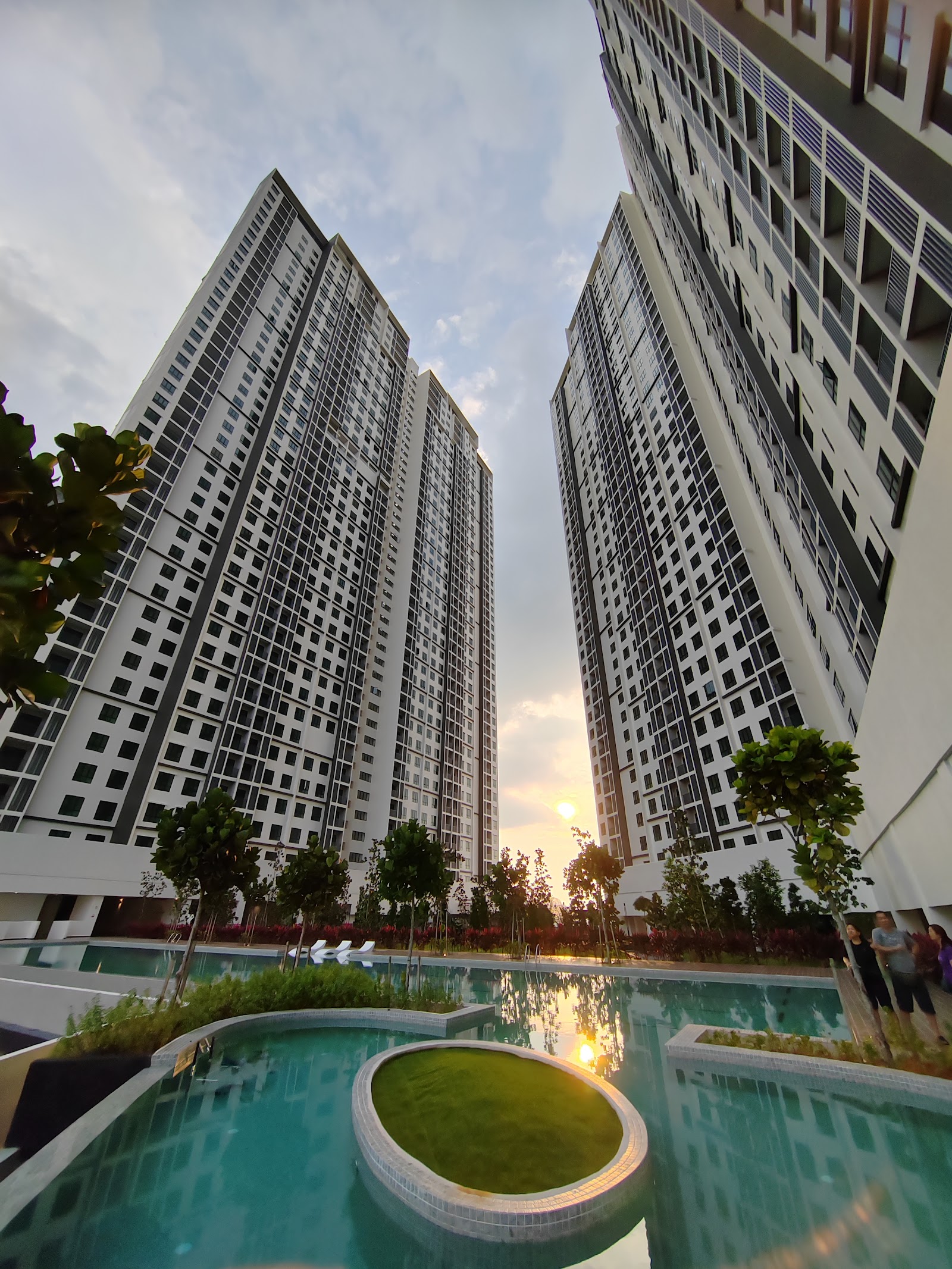 Residensi Bintang Bukit Jalil: A swimming pool and landscaped garden with a circular planter, set within the grounds of a residential development with high-rise towers in the background at sunset.