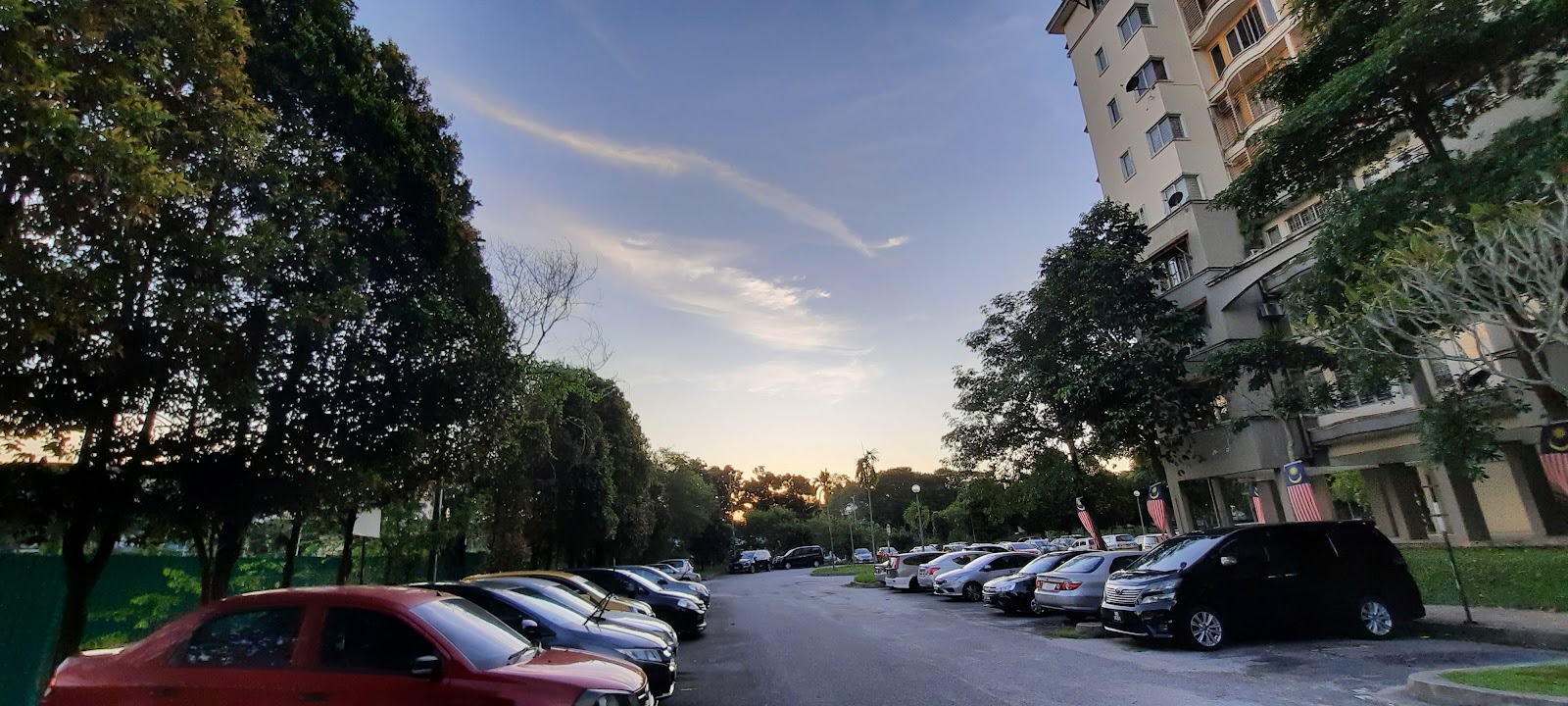 De Rozelle: A parking area with cars lined up next to an apartment building and trees at dusk.