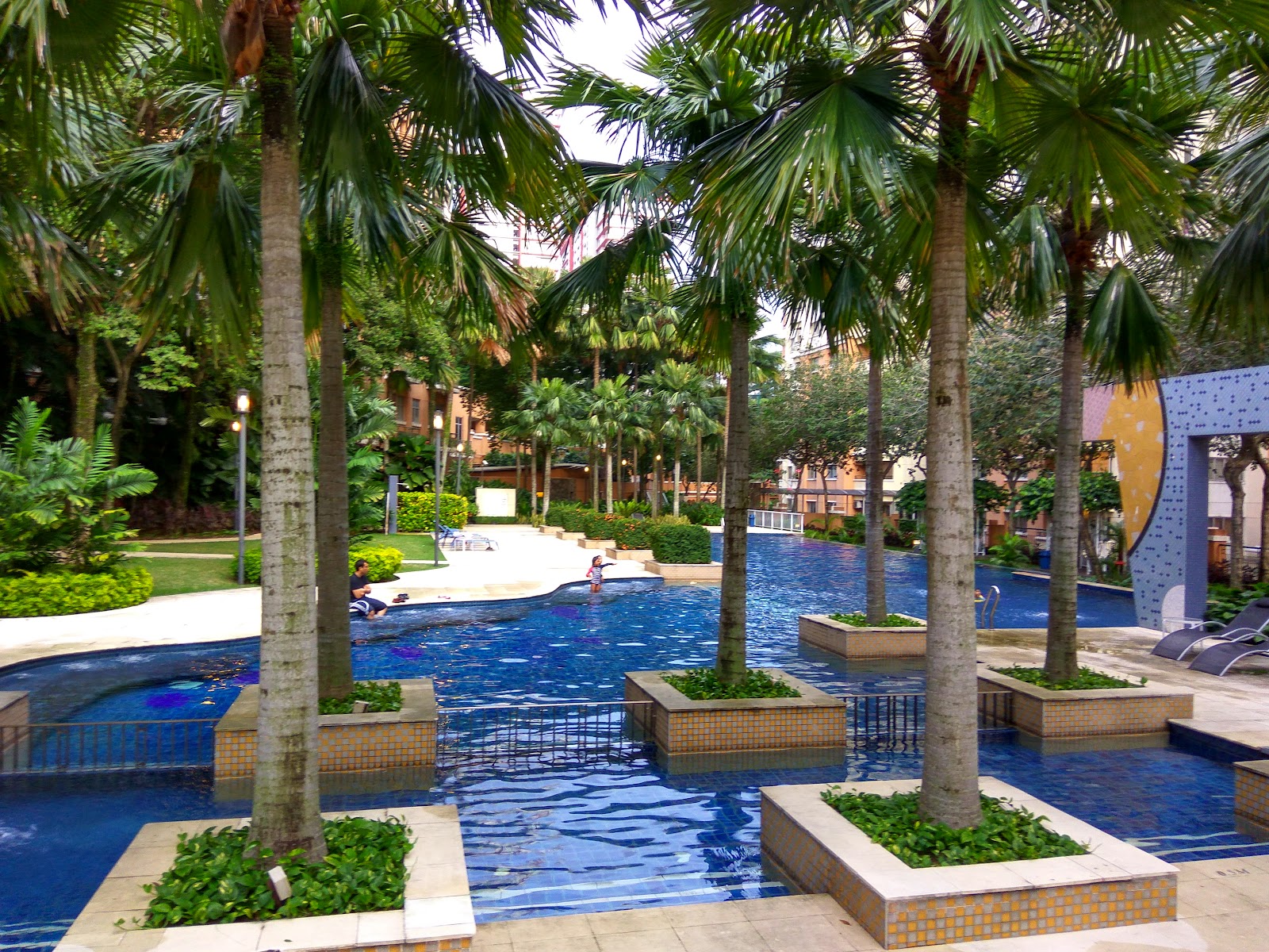 Emerald Serviced Apartment: A landscaped swimming pool area with palm trees and tiled planter boxes.