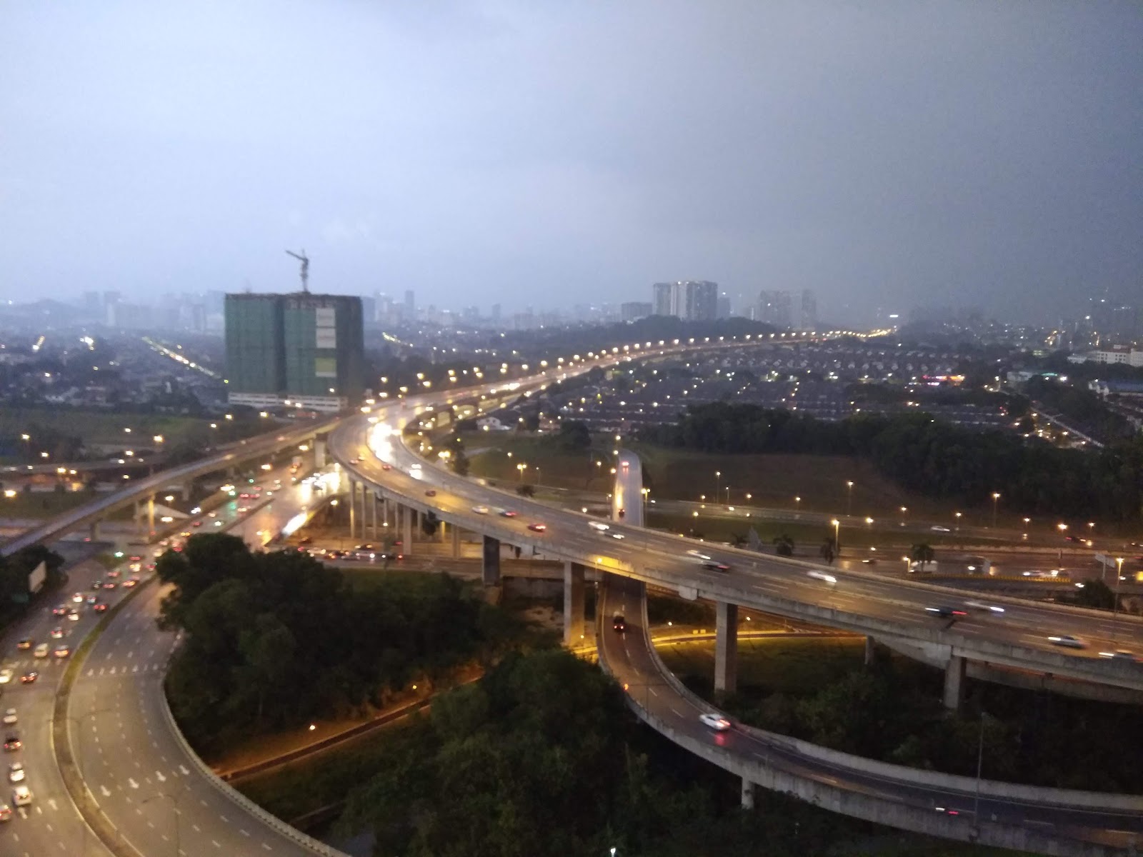 Vista Komanwel: An elevated view overlooking a large highway interchange and the surrounding cityscape at dusk.