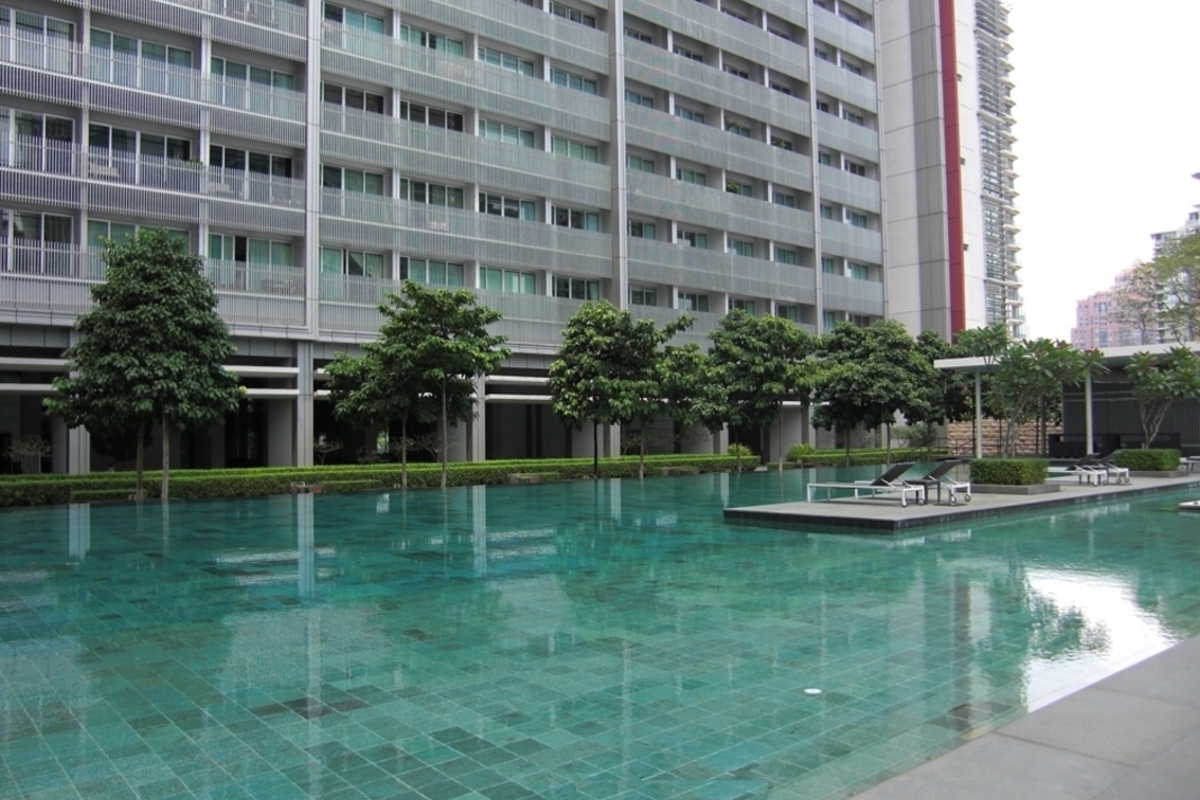 Dua Residency: A swimming pool with turquoise water and a small floating platform with lounge chairs in front of a modern high-rise building.