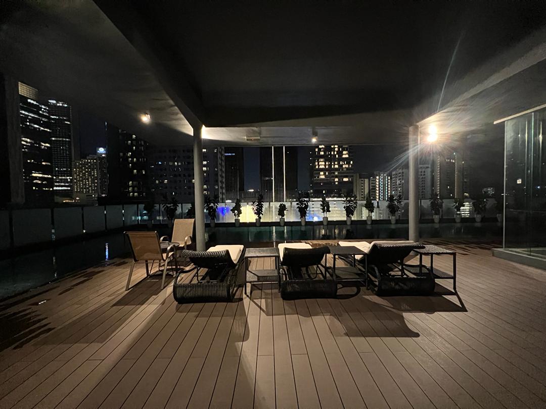 Dedaun Condominium: A night view of a rooftop infinity pool with lounge chairs, set against a city skyline.