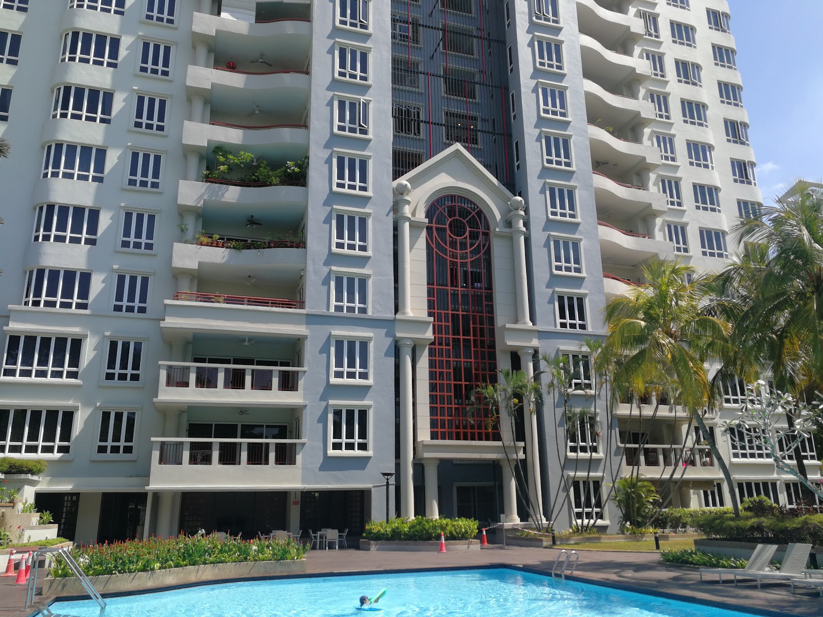 Tara Condominium: A blue swimming pool in the foreground with a swimmer in it, set against the facade of a large, light-colored residential building with balconies and palm trees.