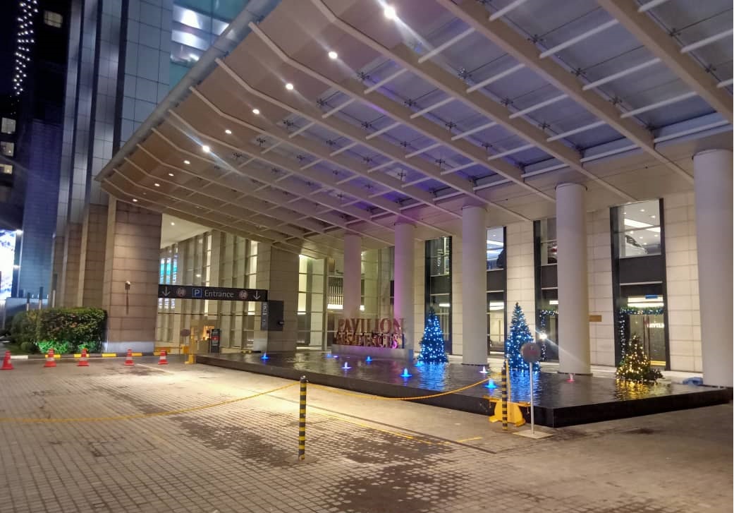 Pavilion Residences: The night-time exterior of the building entrance featuring a large canopy, columns, and a fountain area decorated with blue Christmas trees.