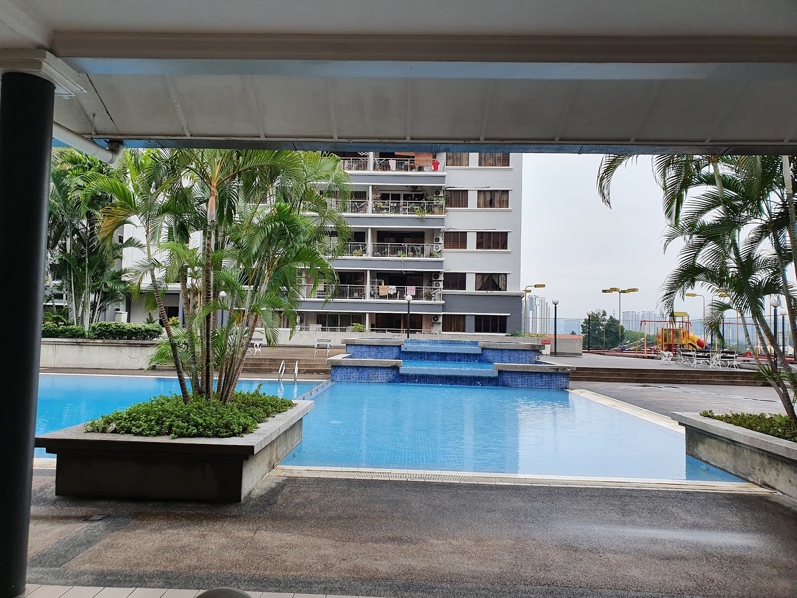 Menara Duta 1: A wide-angle view of an outdoor swimming pool with mosaic tiling and tiered steps, set in the landscaped courtyard of a residential building.