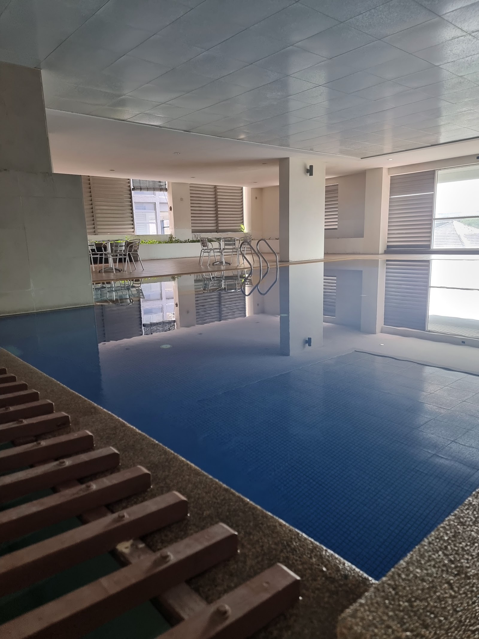 Taragon Puteri YKS: An indoor swimming pool with a wooden deck area containing chairs and a metal handrail.