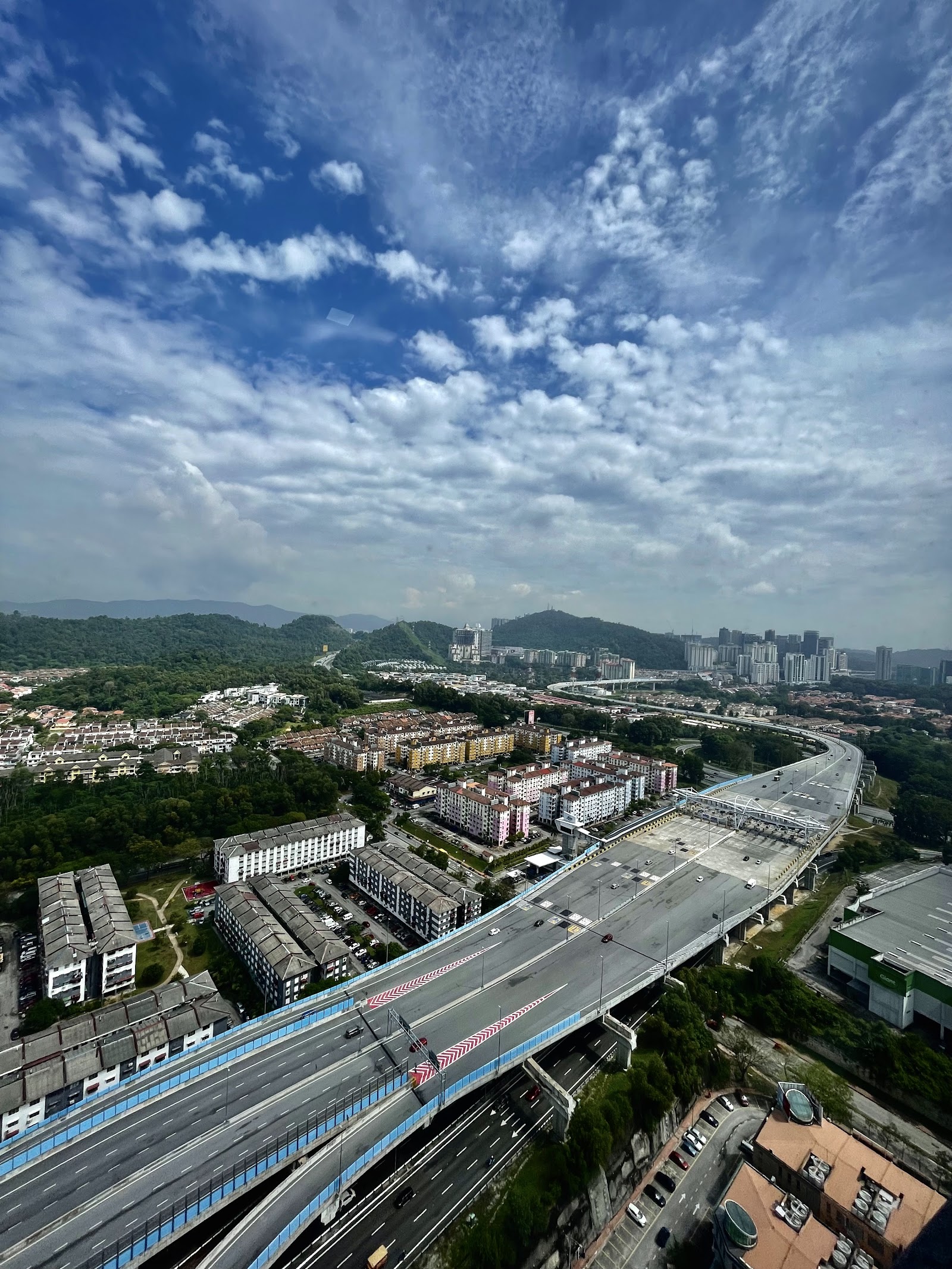 Encorp Strand Residences: A high-angle view of a city with a major highway, residential blocks, and green hills in the background under a cloudy sky.