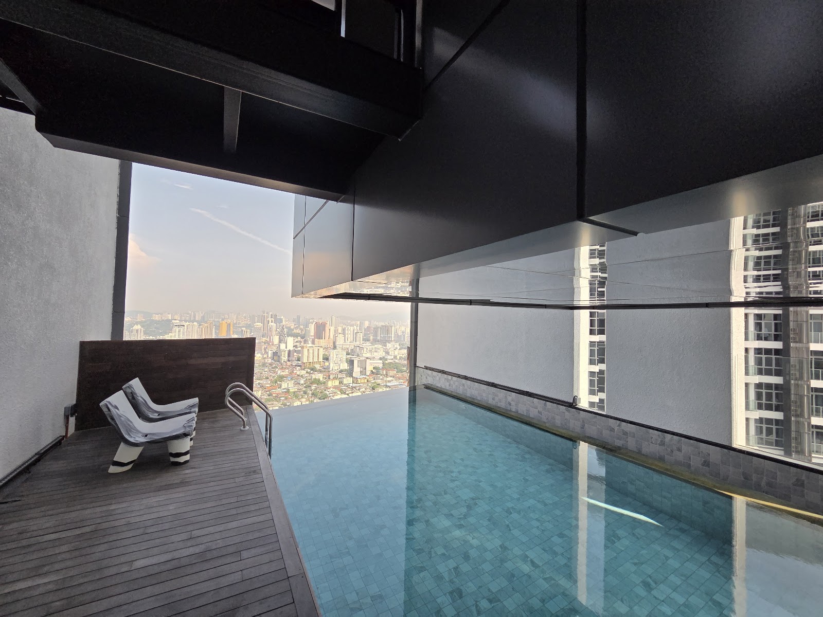 Isola KLCC: A high-level rooftop infinity pool with a wooden deck and lounge chairs, overlooking a sprawling cityscape.
