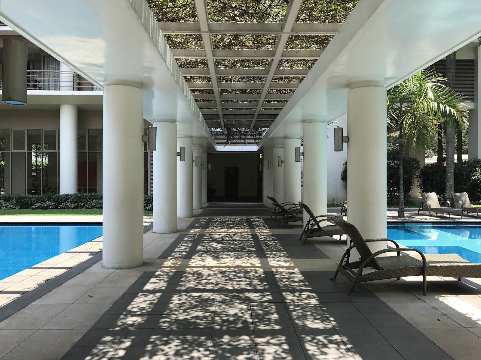 Hampshire Park: A covered walkway with white columns lining a swimming pool, featuring lounge chairs and a trellis roof.