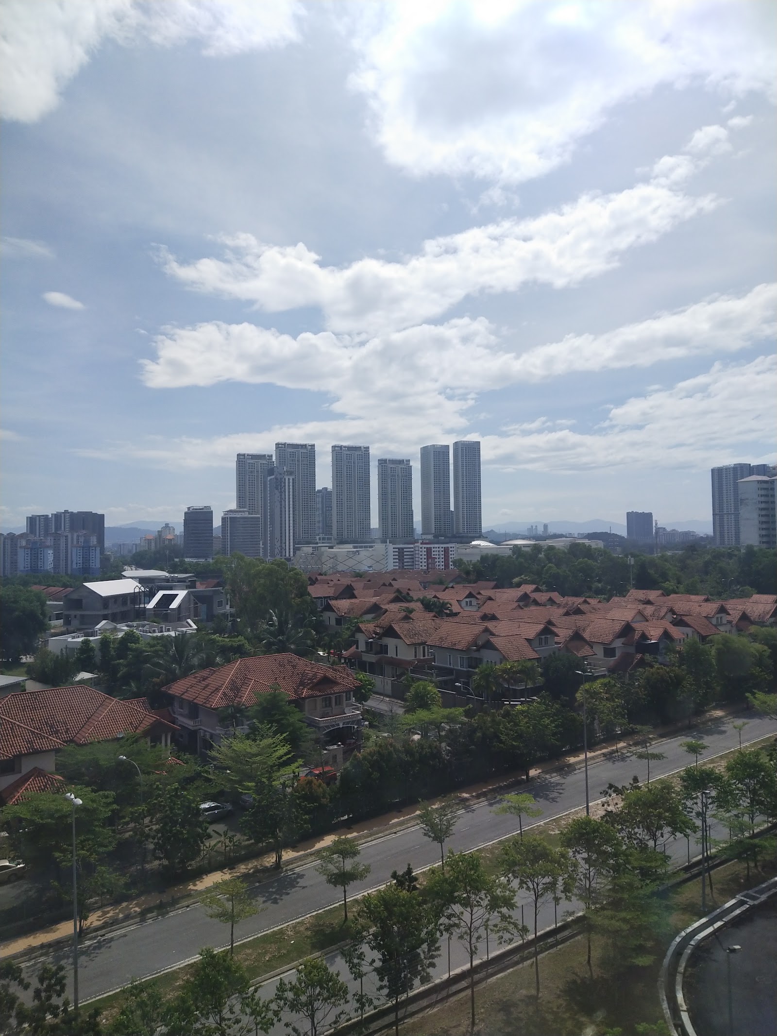 Condominium Akasia Bukit Jalil: An elevated view looking out over a residential area with houses and a road, with a city skyline of high-rise buildings in the distance under a cloudy sky.
