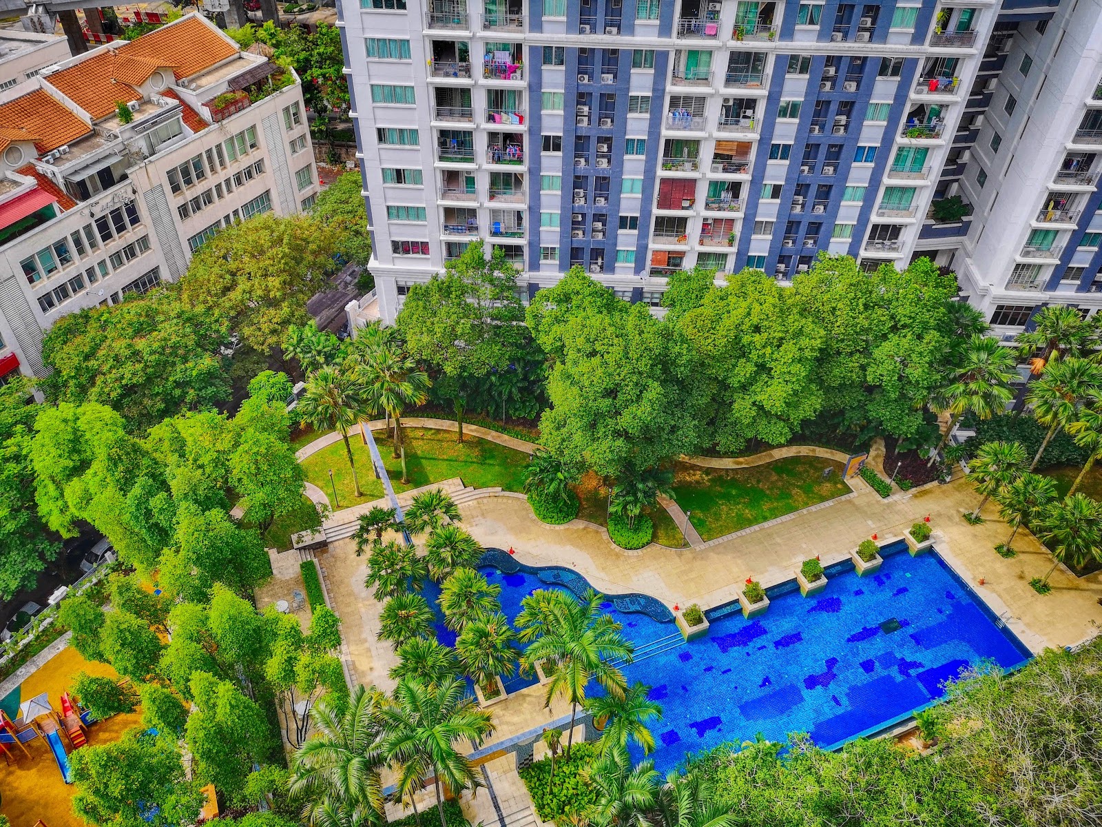 Emerald Serviced Apartment: An aerial view of a swimming pool and landscaped garden area with palm trees, set against a backdrop of an apartment building.
