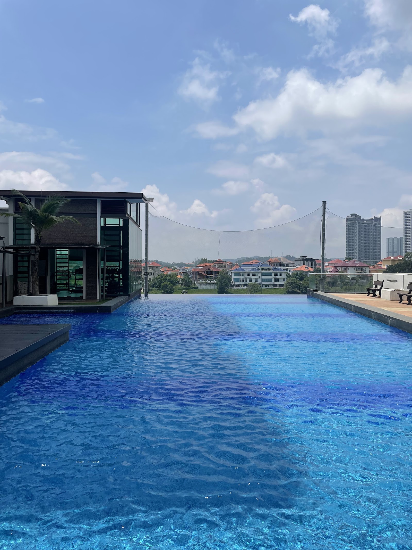 Savanna: A rooftop infinity pool with lounge chairs at the edge, looking out over a neighborhood of houses and distant high-rise buildings under a blue sky.