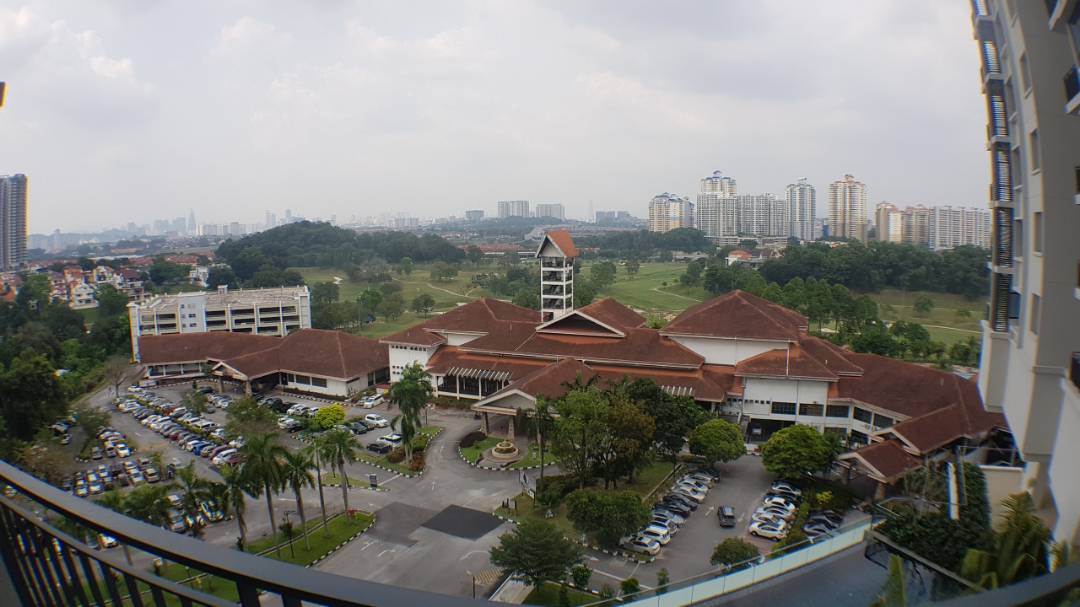 The Link 2: A view from a balcony looking over a large red-roofed building with parking lots and green fields towards a distant city skyline.