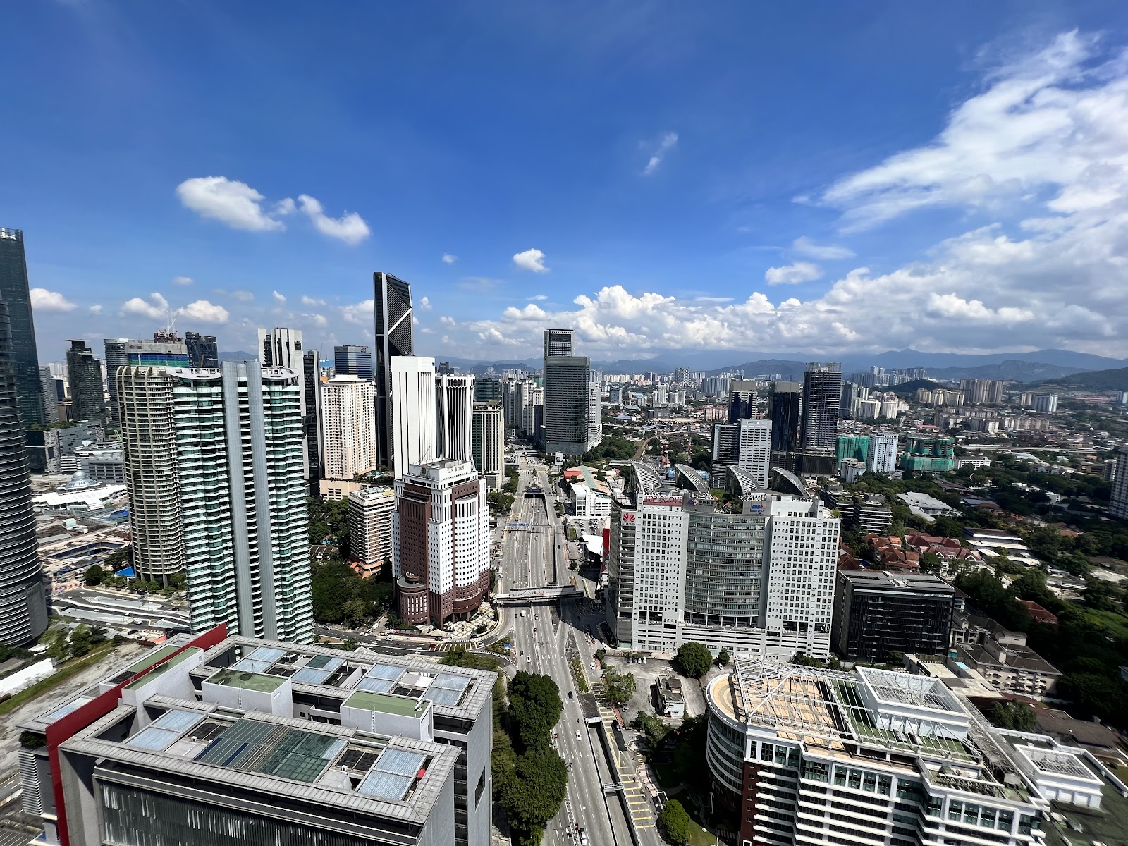 ARIA Luxury Residence: An elevated, wide-angle view of a city skyline with high-rise buildings and a major road under a blue sky with clouds.