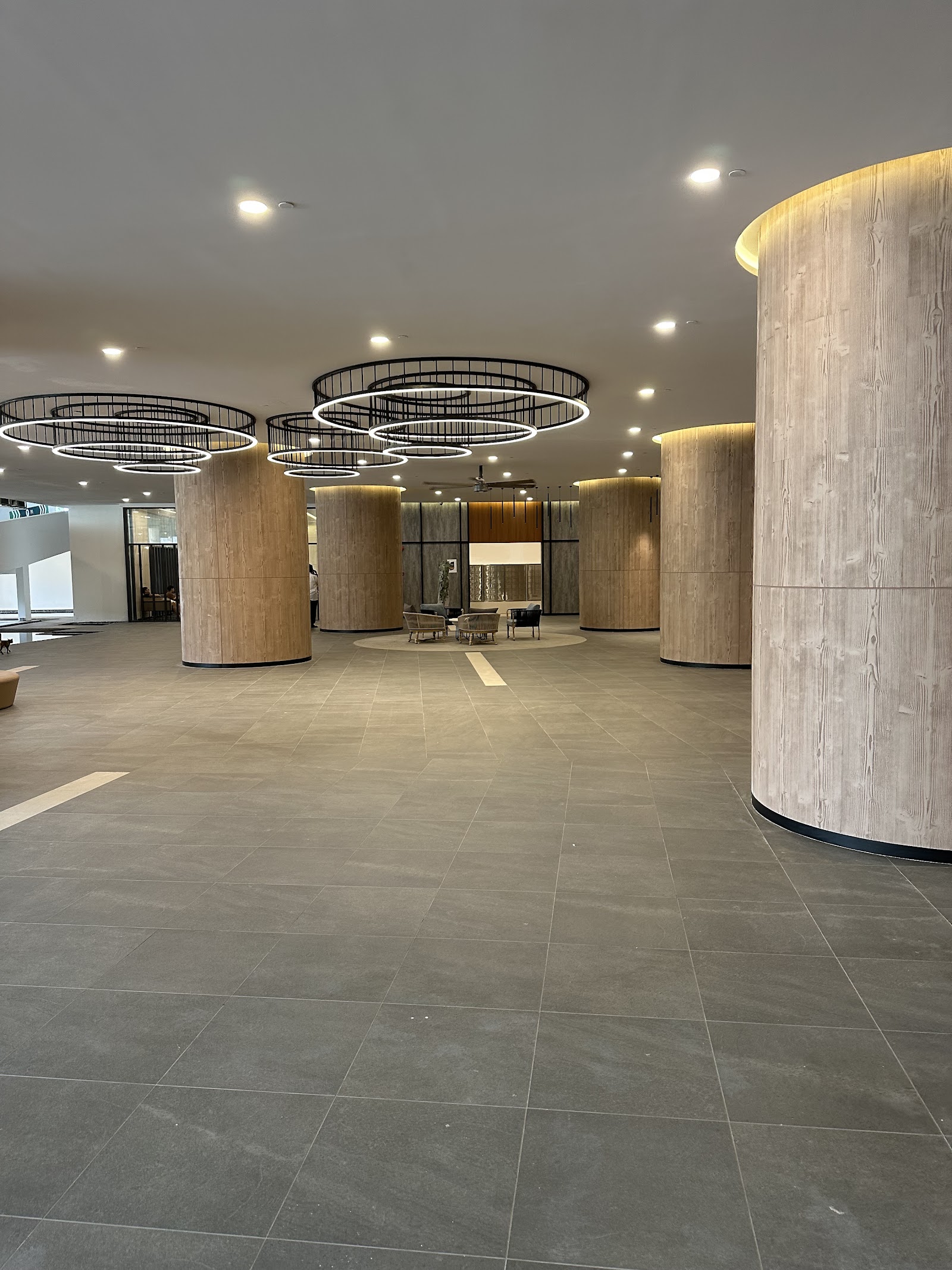 SUNWAY D'HILL RESIDENCES, PETALING JAYA: A spacious interior lobby with wooden cylindrical columns, grey floor tiles, and hanging circular ring chandeliers.
