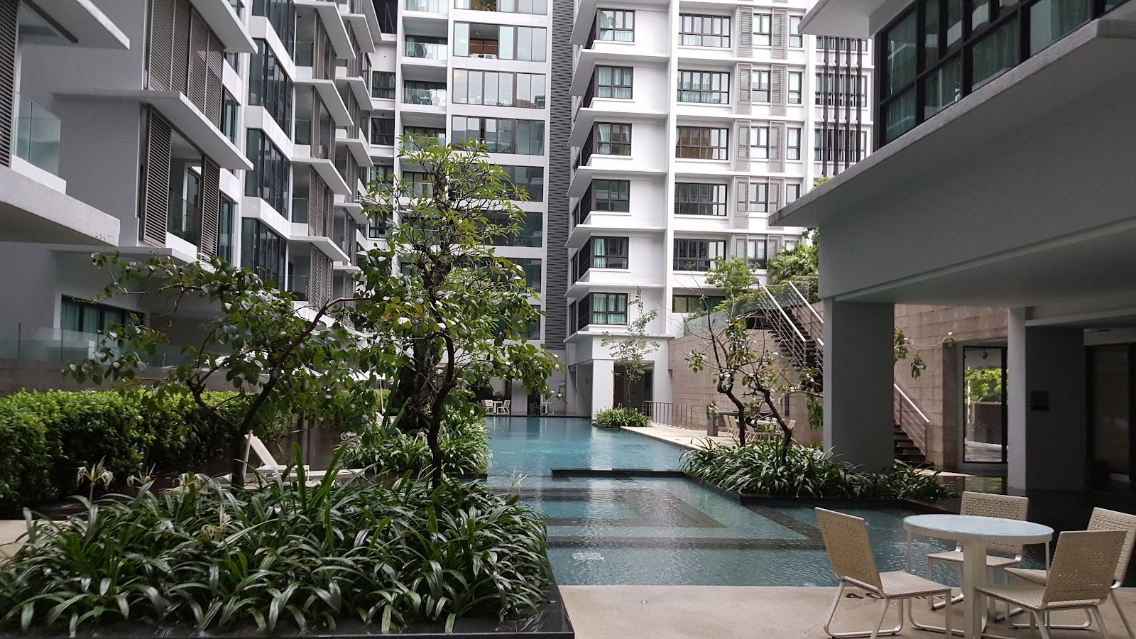 Sastra U-Thant: An outdoor swimming pool with a small patio area and chairs, surrounded by greenery and tall residential buildings.