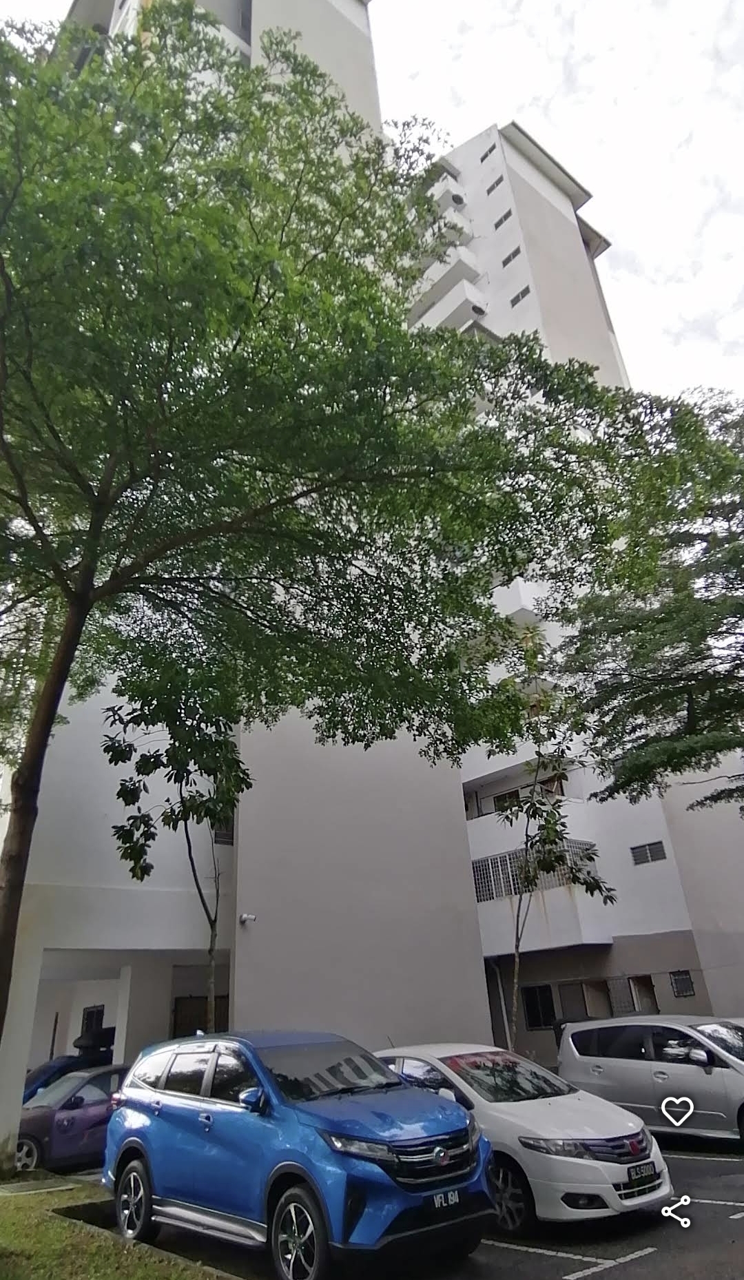 Apartment Seri Ceria 1: An exterior view of a high-rise residential building, showing its white facade and ground level with cars parked in the foreground.