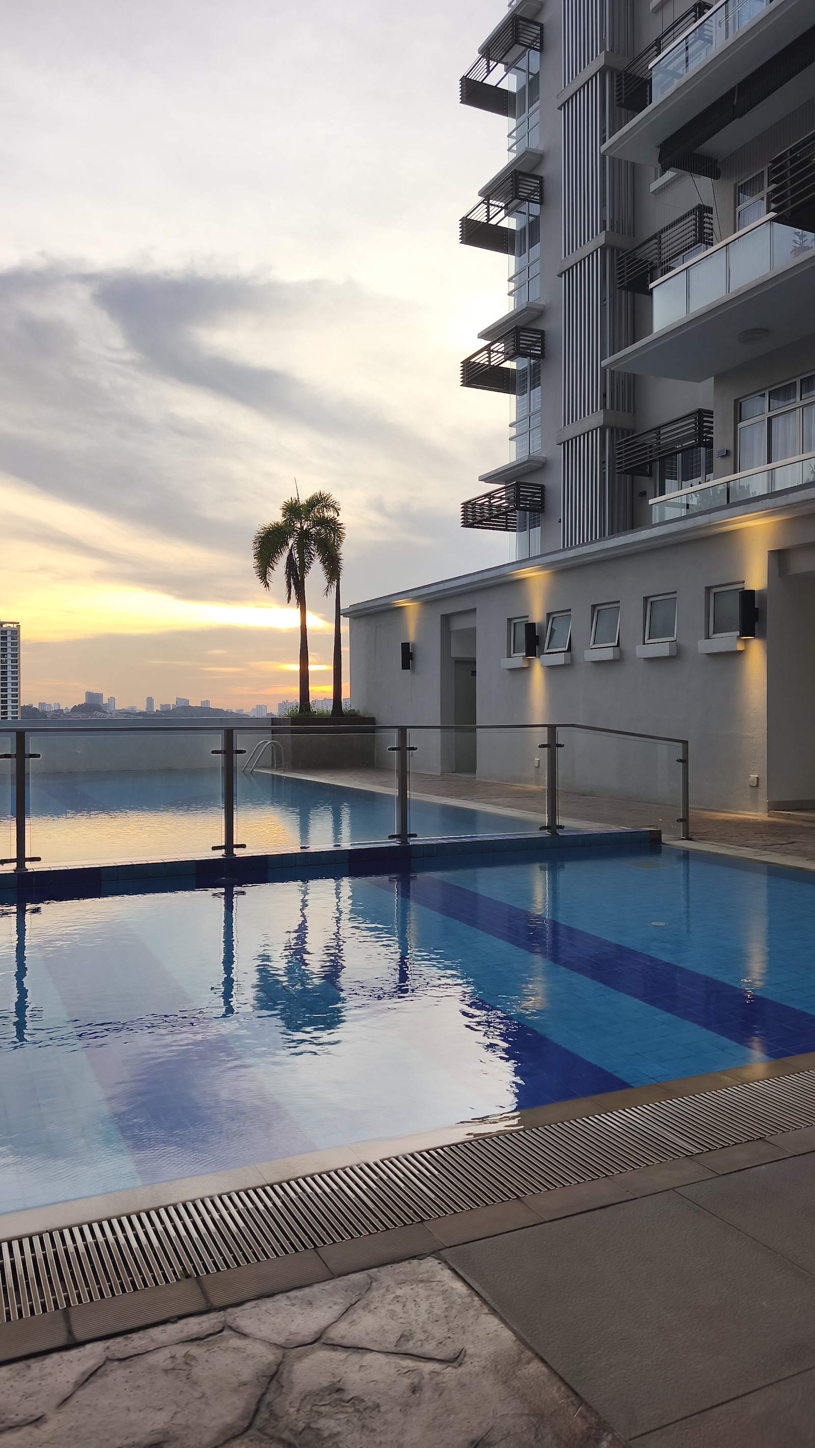 Residensi Bukit Jalil: A rooftop swimming pool with blue lane markings, next to a building wing, looking out over the city skyline at sunset.