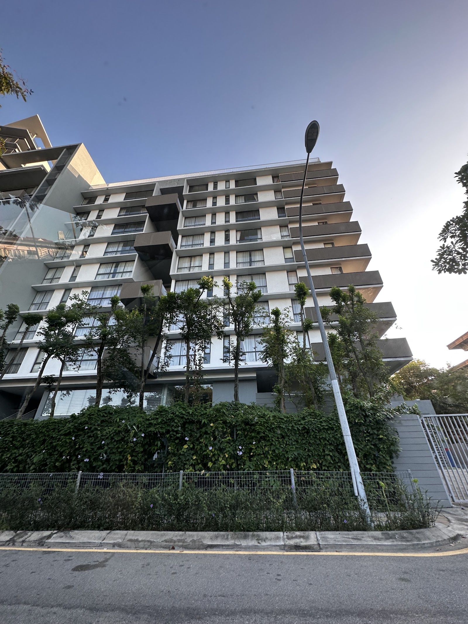 Katana II: A modern residential building with white facades, dark balconies, and landscaping at the base, viewed from a street.