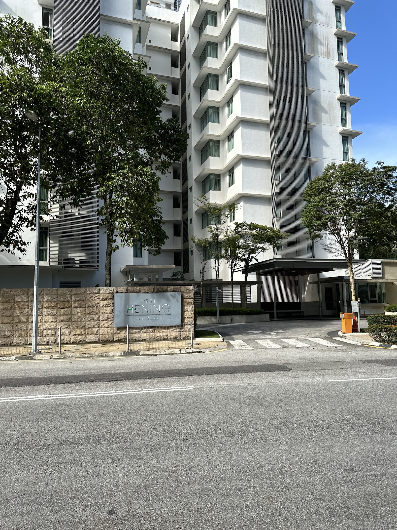 Seri Hening Residence: The street-level entrance and facade of the Seri Hening Residence building, featuring a stone boundary wall, signage, and landscaped grounds.