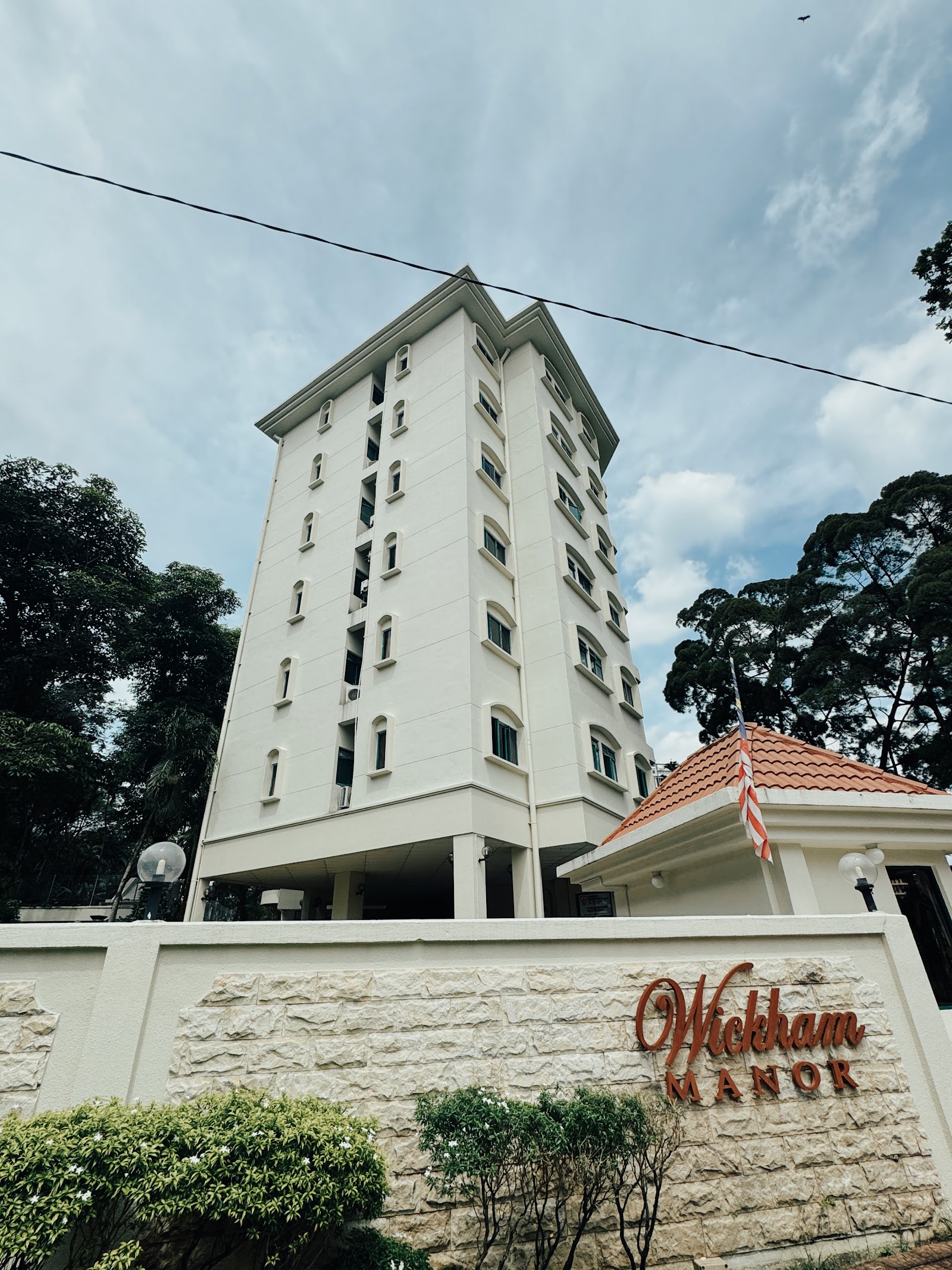 Wickham Manor: The exterior of a tall, white residential tower and a tiled-roof entrance structure, with a 'Wickham Manor' sign on the perimeter wall.