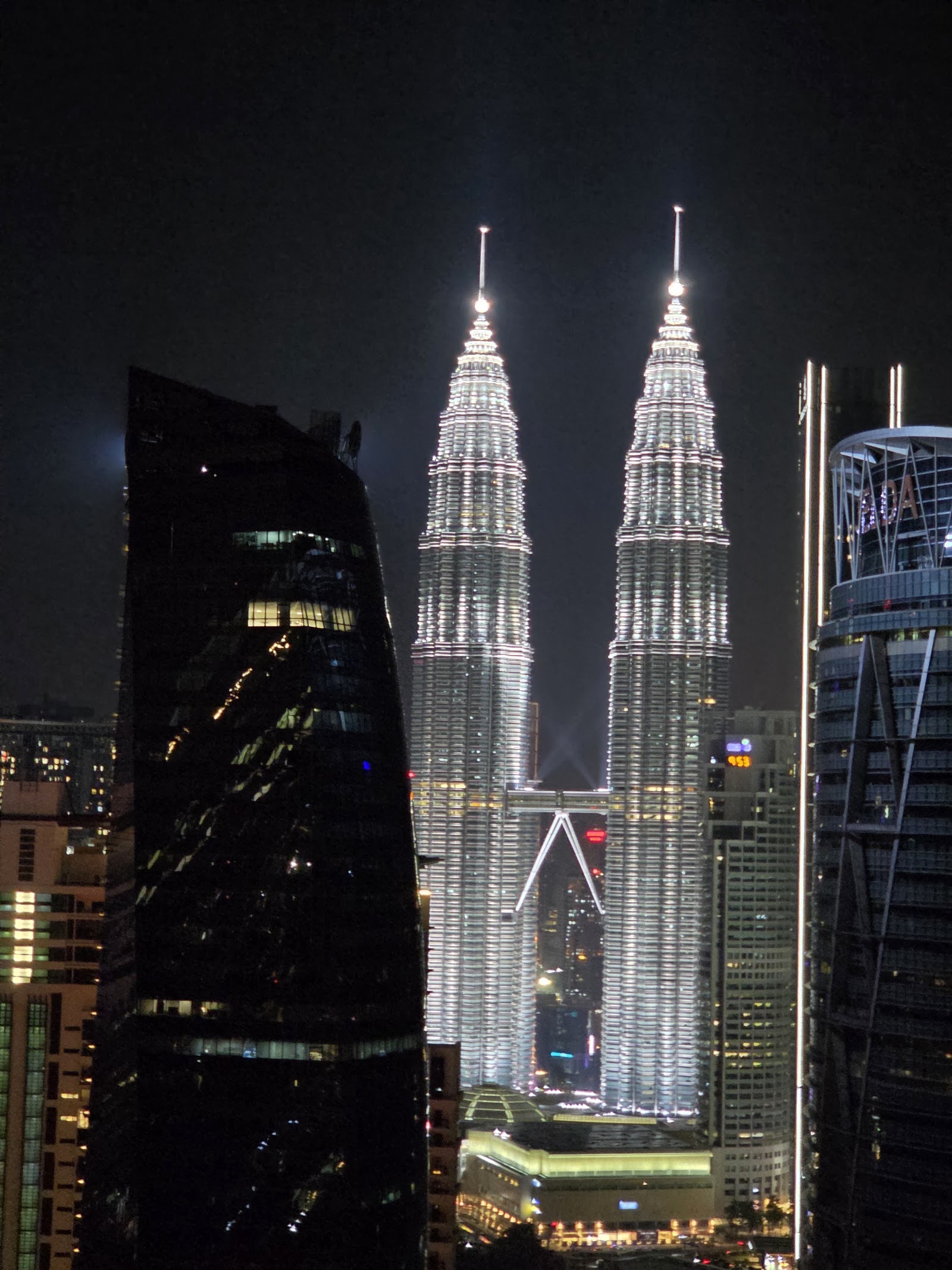 10 Stonor: A night view of the Petronas Twin Towers and surrounding buildings in Kuala Lumpur, seen from across the street or a nearby building.