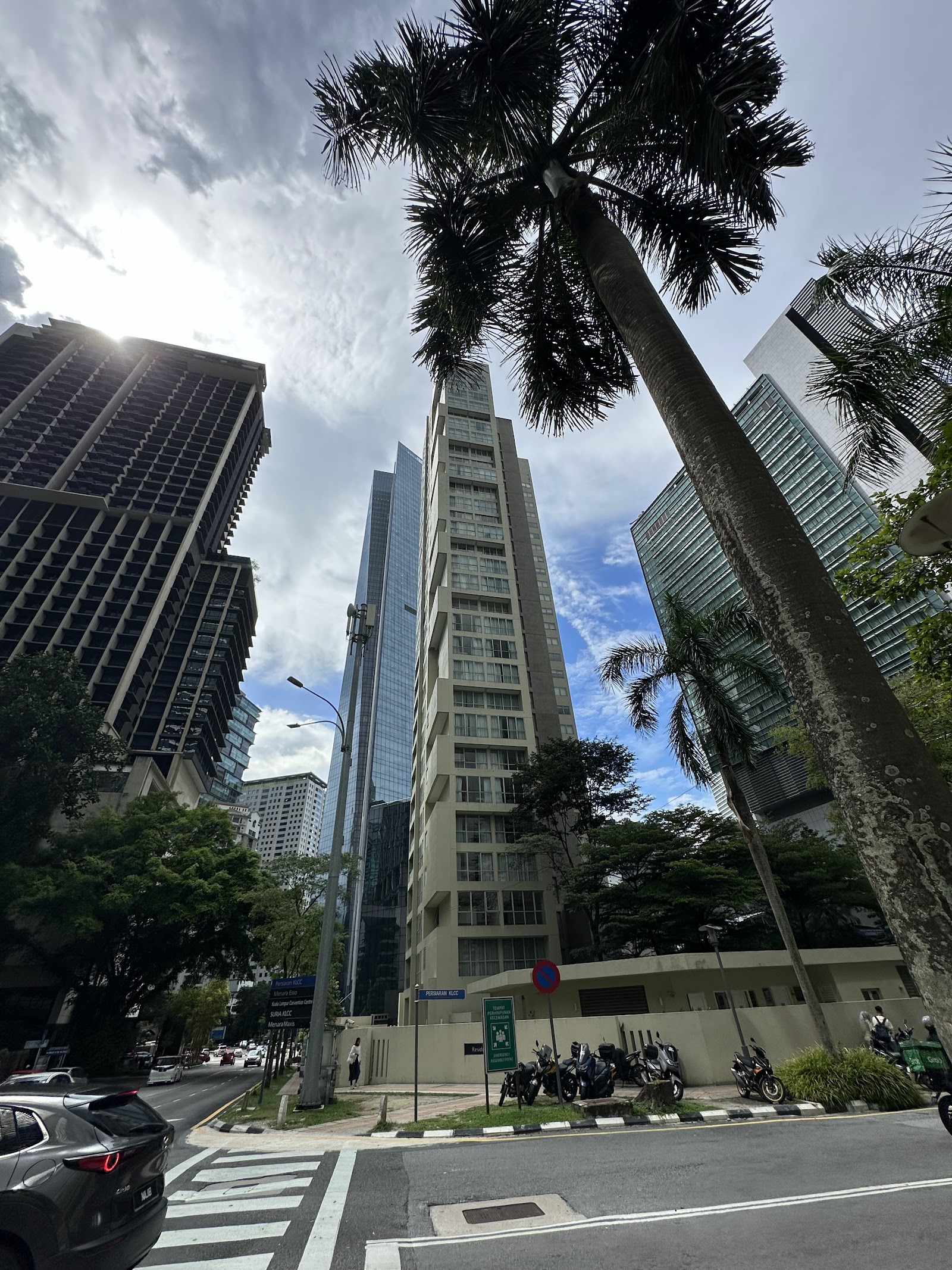 Residensi Kia Peng: A street-level view of a cluster of high-rise residential buildings and office towers, framed by palm trees and surrounded by city traffic.