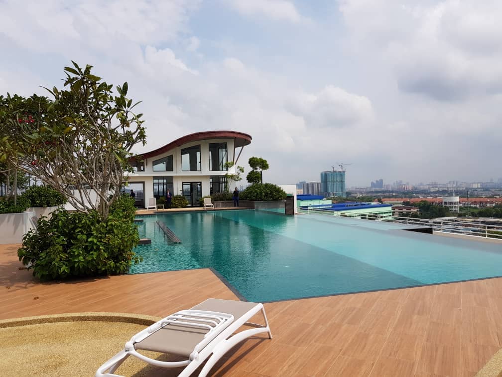 Denai Sutera: An infinity pool on a rooftop terrace with wooden decking and a lounge chair, overlooking a city skyline.