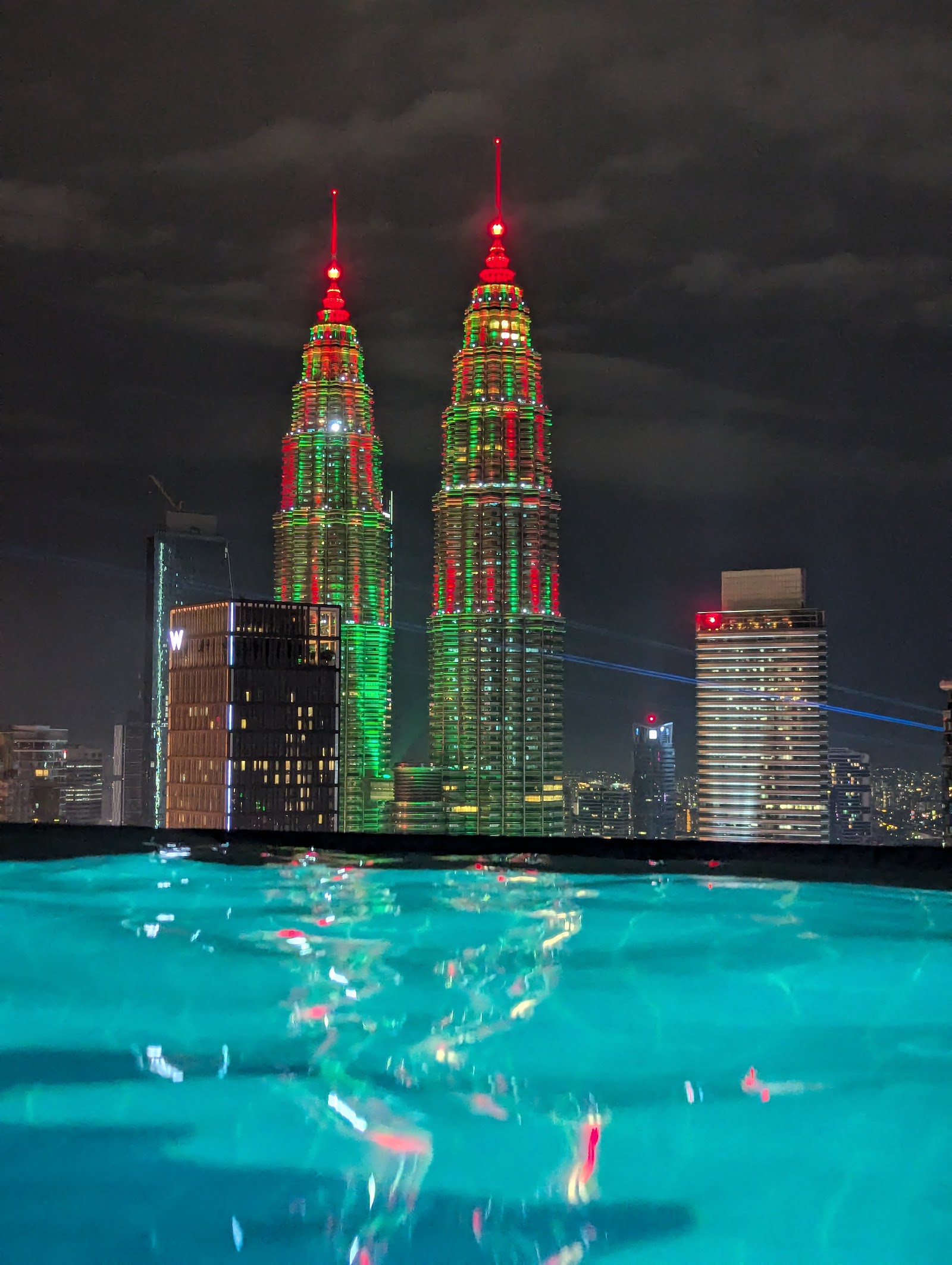 Platinum Victory Suites: A view from a rooftop infinity pool at night, looking out over the city skyline with the illuminated Petronas Twin Towers.