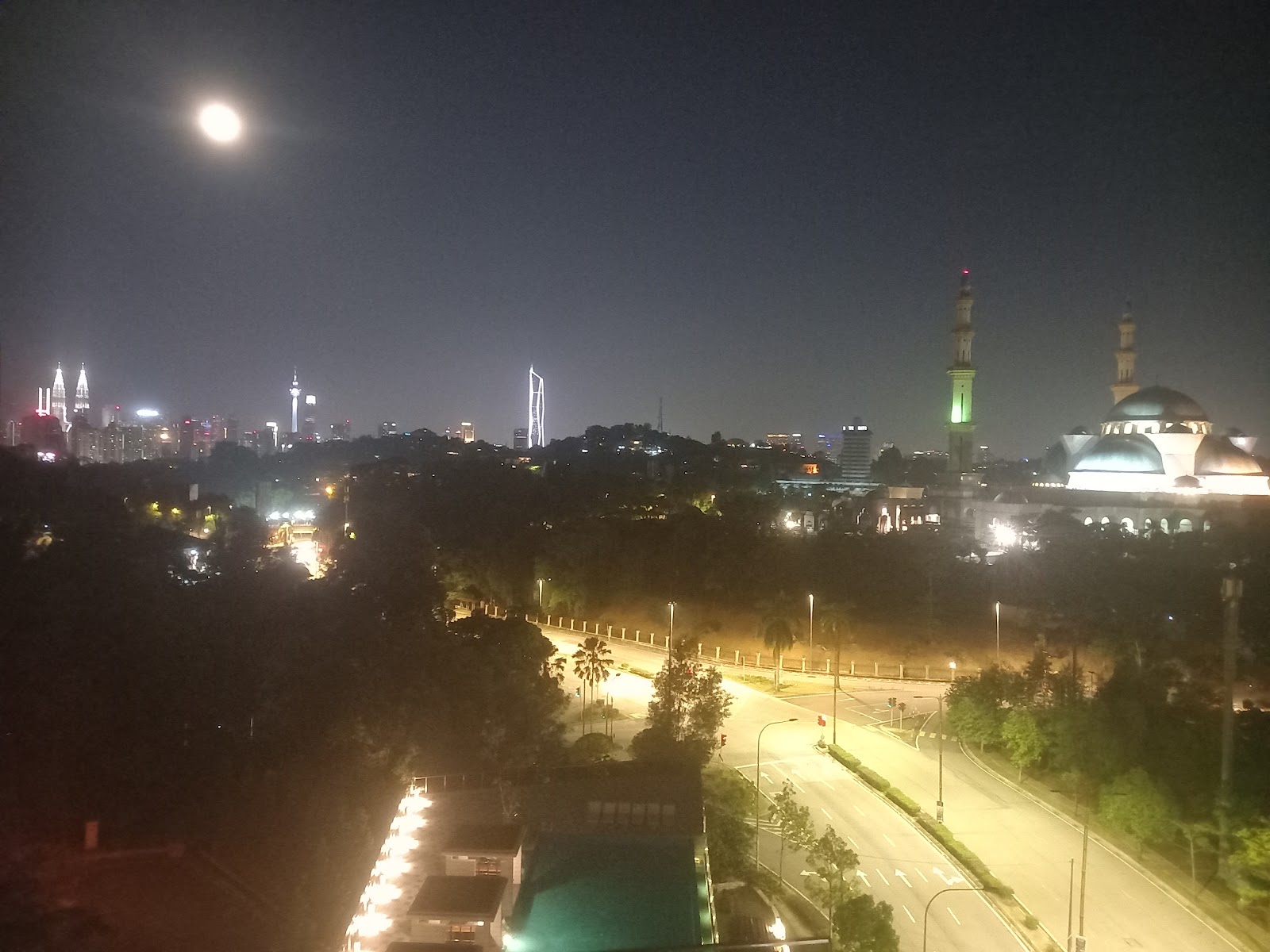 Met 1 Residences: A night view of a city skyline featuring lit skyscrapers and a large mosque, taken from an elevated position.