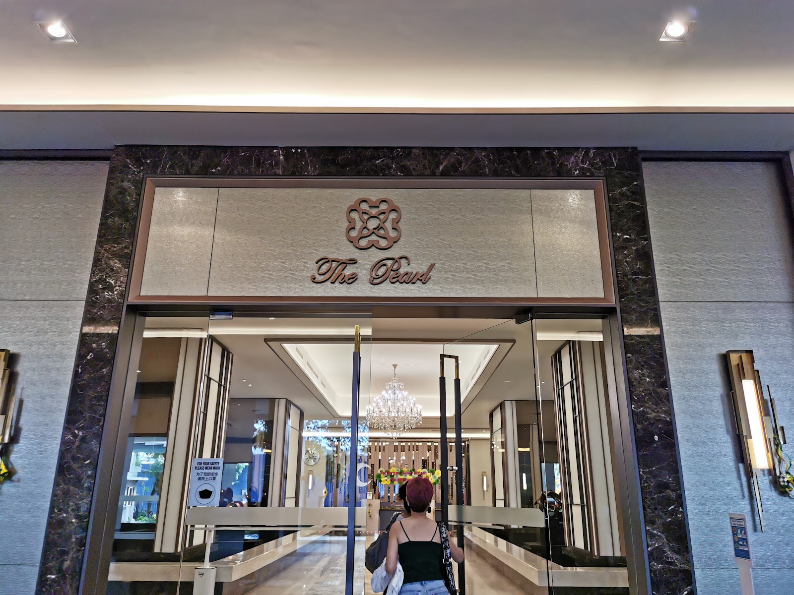 The Pearl: A woman is entering The Pearl through glass doors into a lobby featuring a large crystal chandelier.