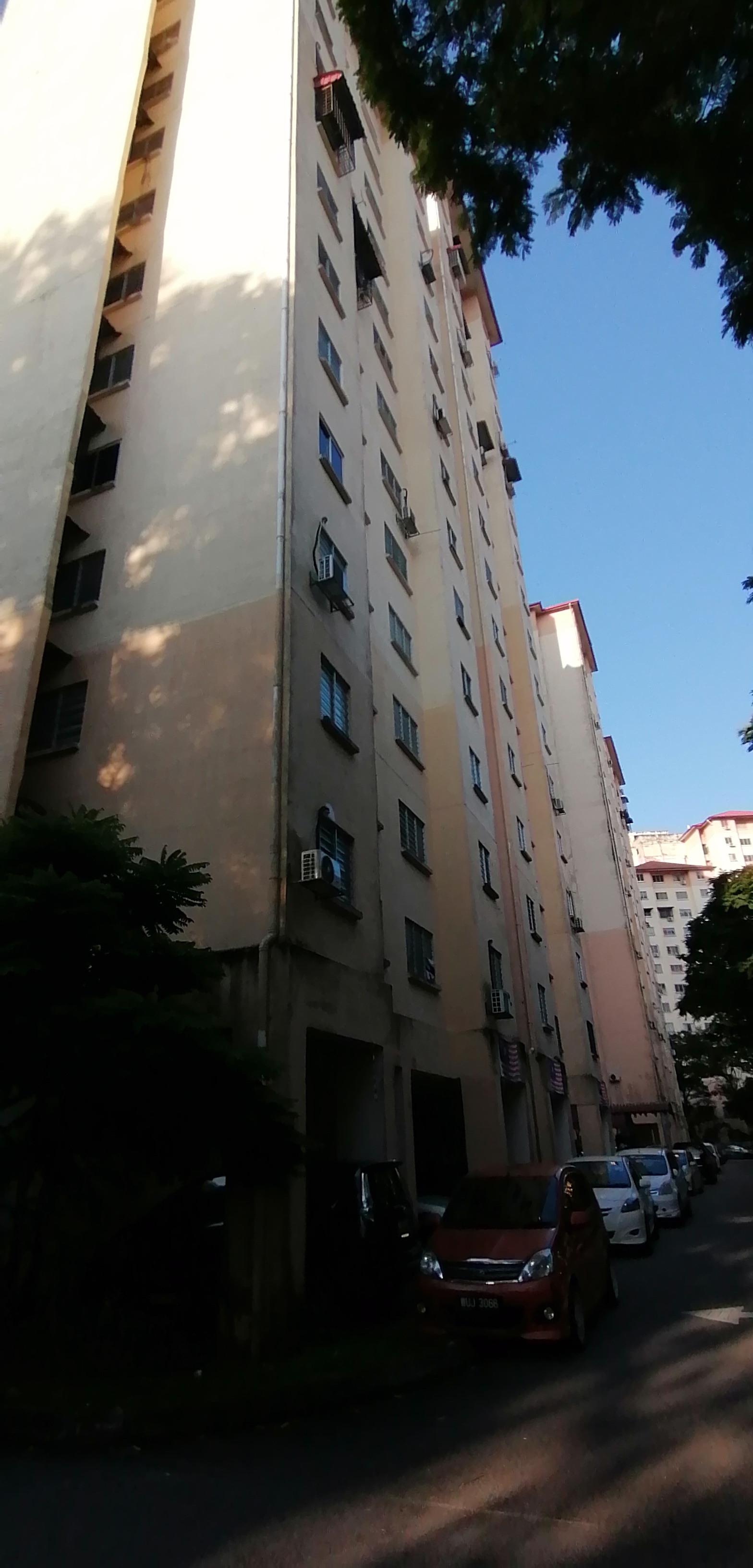 PPR Pinggiran Bukit Jalil: A street-level view of a residential high-rise building facade with cars parked along the side.